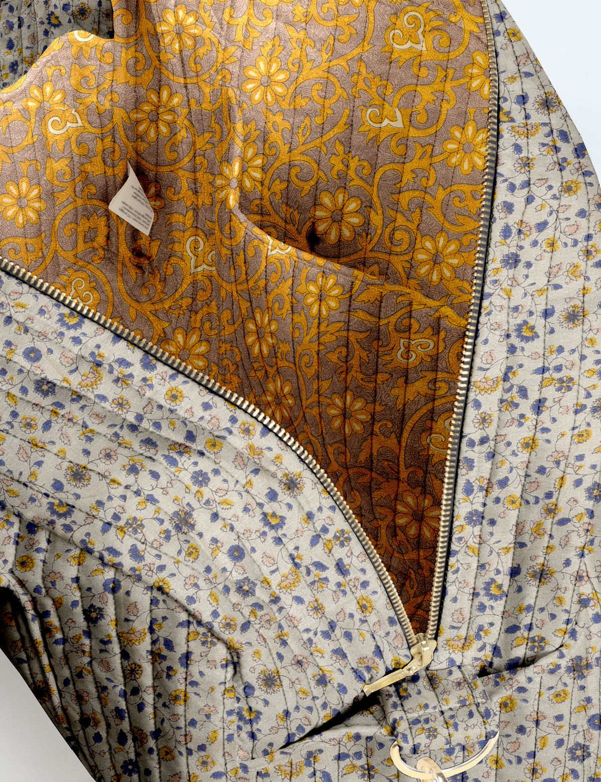 Brown quilted duffle bag with paisley pattern, front zip pocket, dual handles, and label reading "I was a sari"