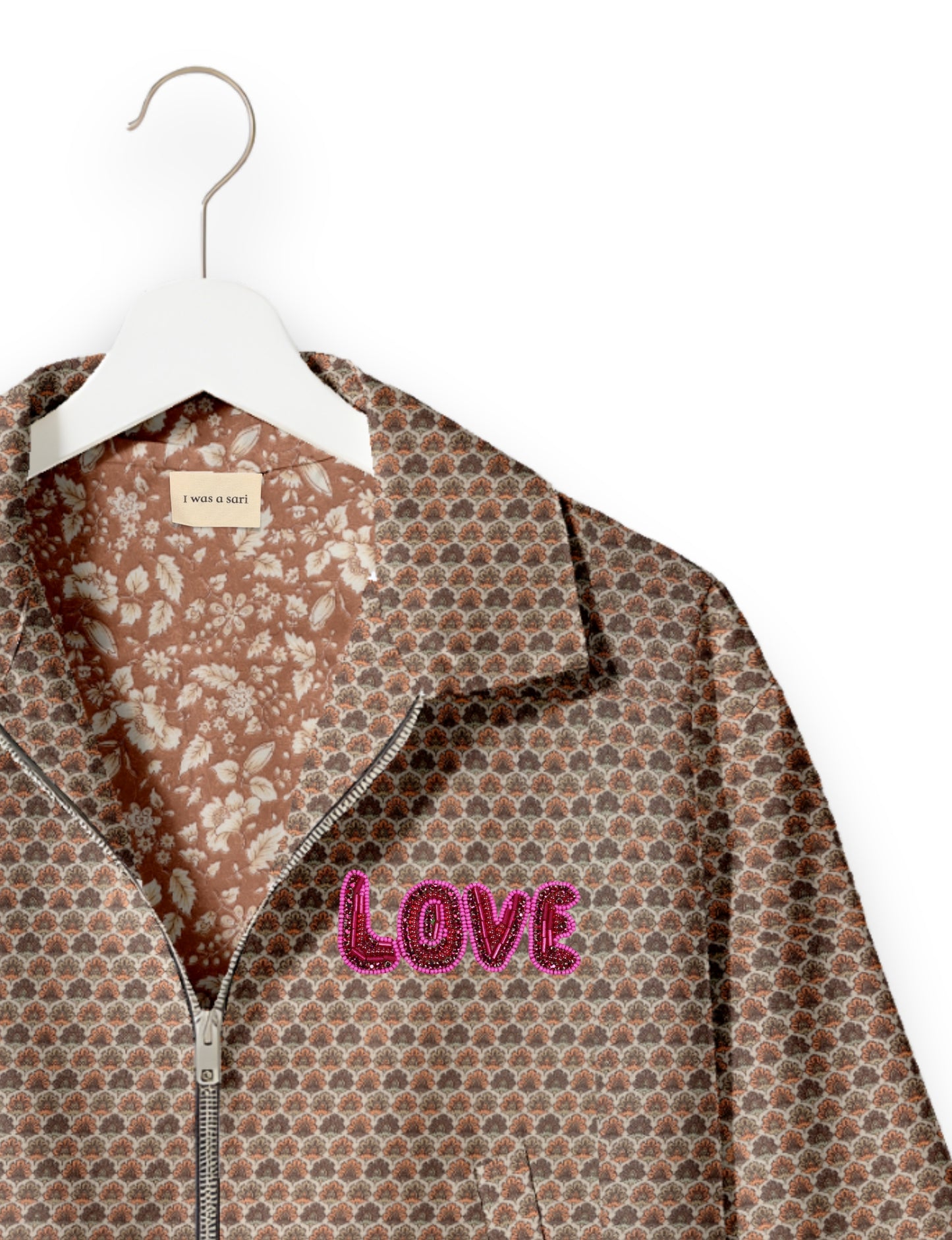 Beige bomber jacket with micro floral pattern, pink beaded "LOVE" patch, floral inner lining, and front zipper on white hanger
