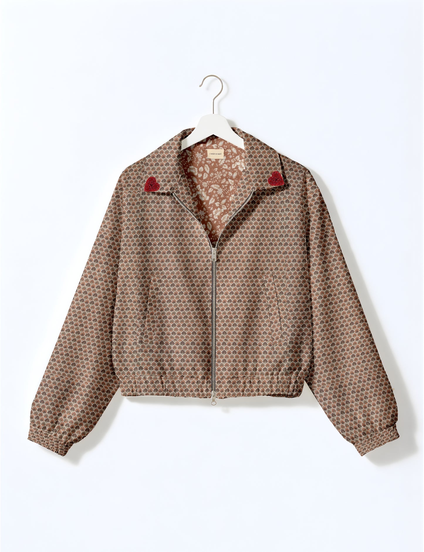 Beige bomber jacket with micro scallop pattern, red heart patches on collar, front zipper, elastic cuffs, and floral inner lining