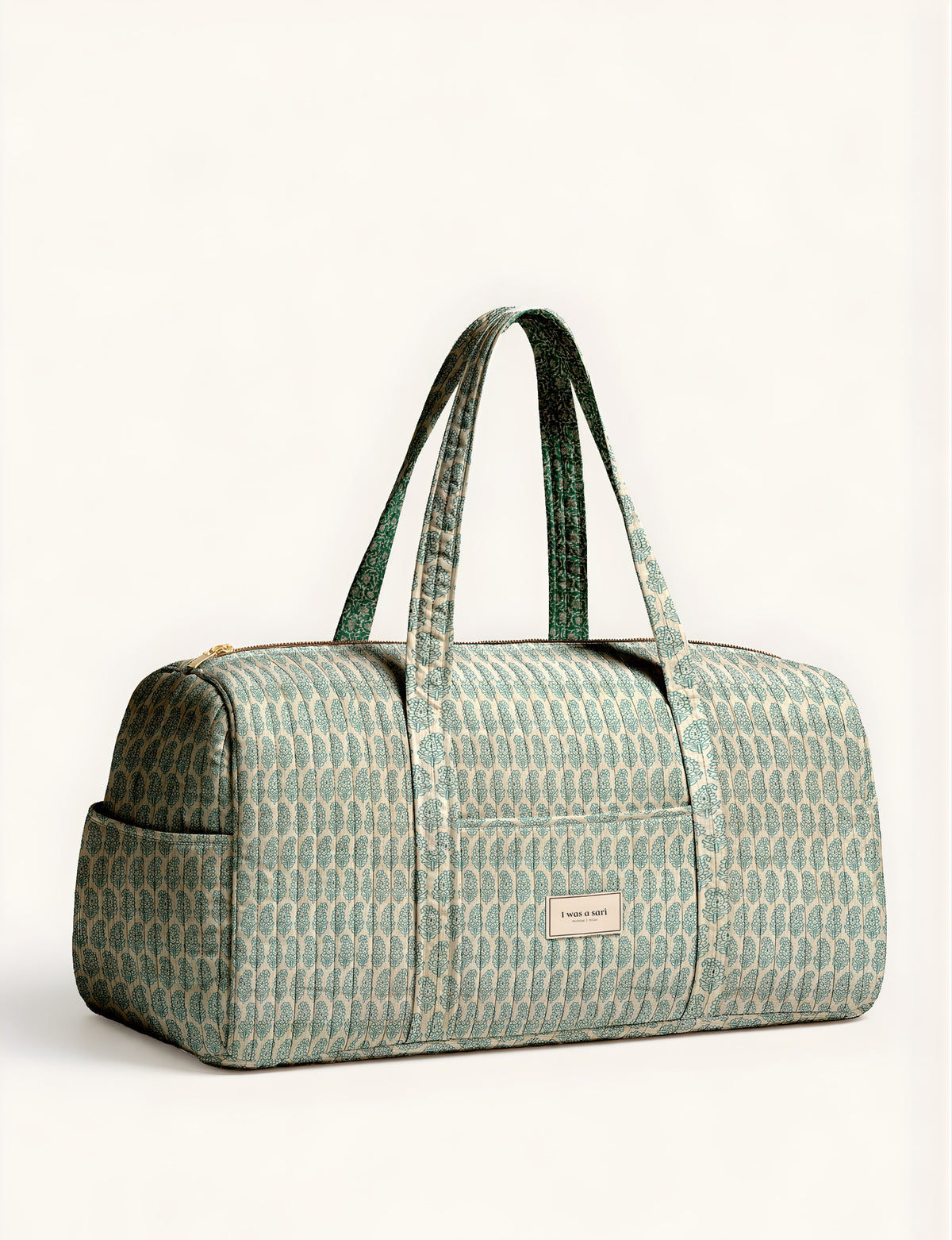 Woman holding a brown paisley quilted barrel bag with front zipper pocket, wearing light blue jeans and white sneakers
