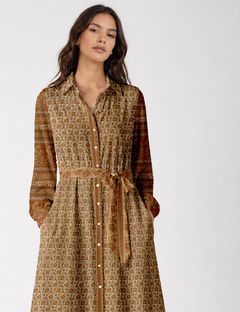 Woman wearing a beige long shirt dress with tropical floral and stripe patterns, button front, waist tie, and long sleeves