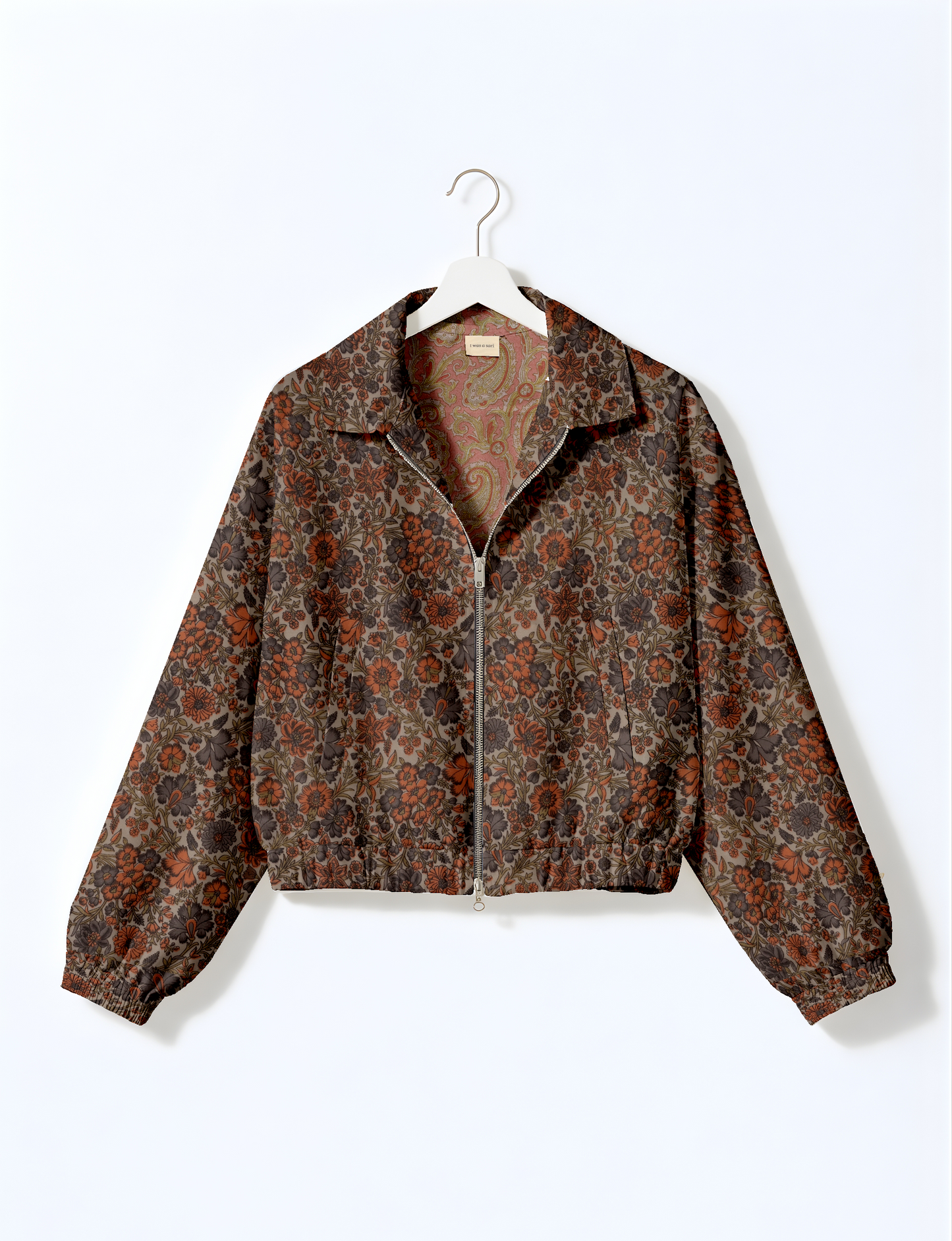 Beige bomber jacket with tropical floral pattern, front zipper, collar, and elastic cuffs, hanging on white hanger