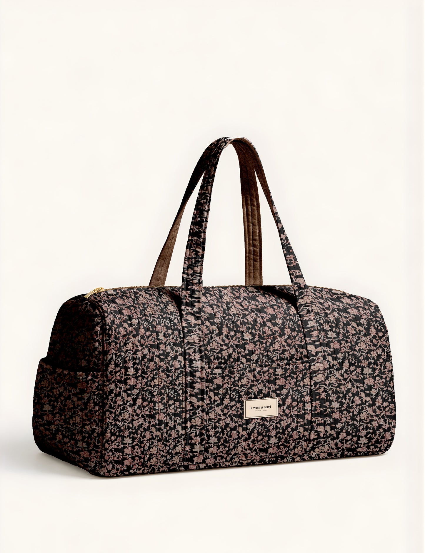 Woman holding a brown paisley quilted barrel bag with front zipper pocket, wearing light blue jeans and white sneakers