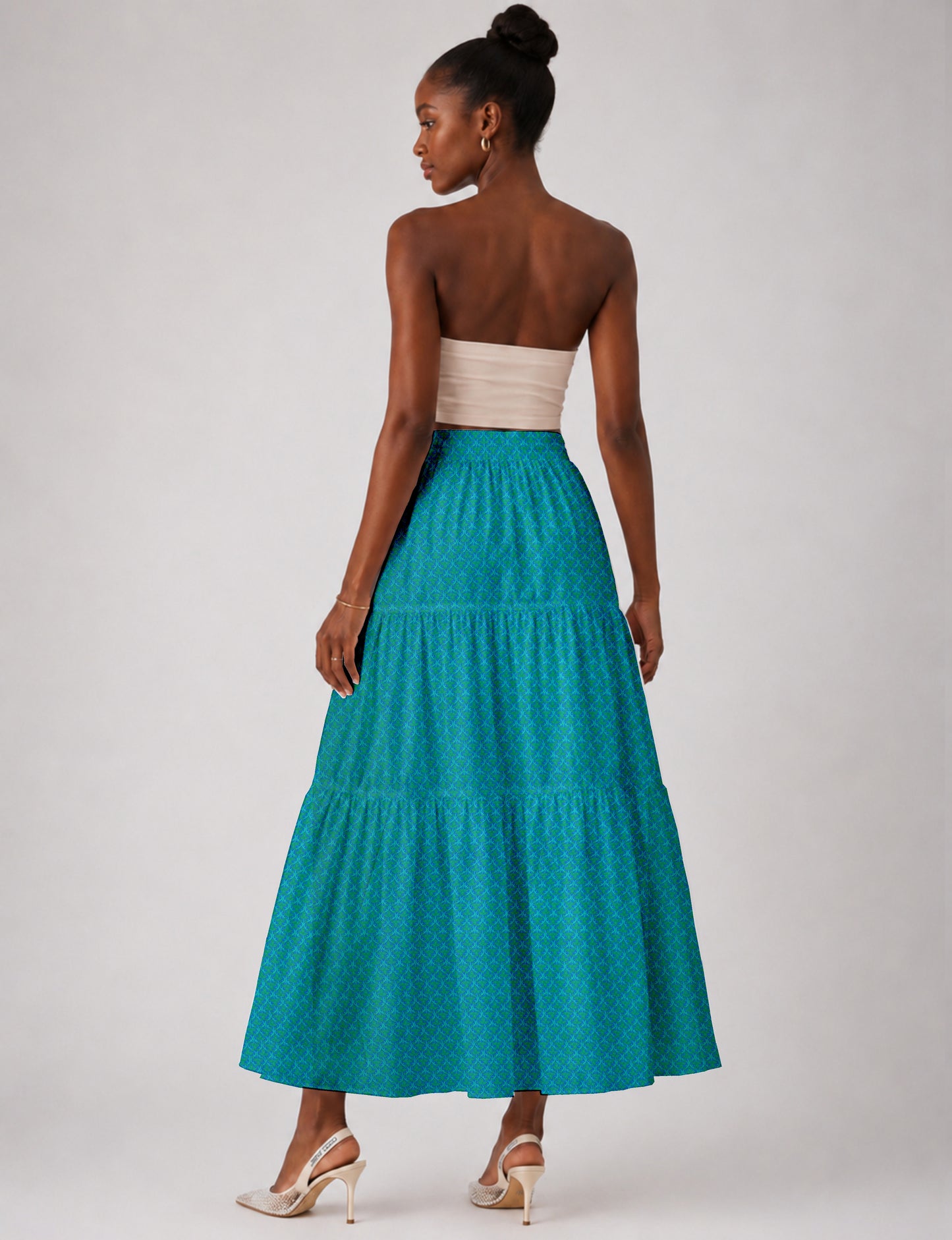 Woman wearing a blue midi tiered skirt with a micro pattern, paired with a beige strapless top and beige high heels, back