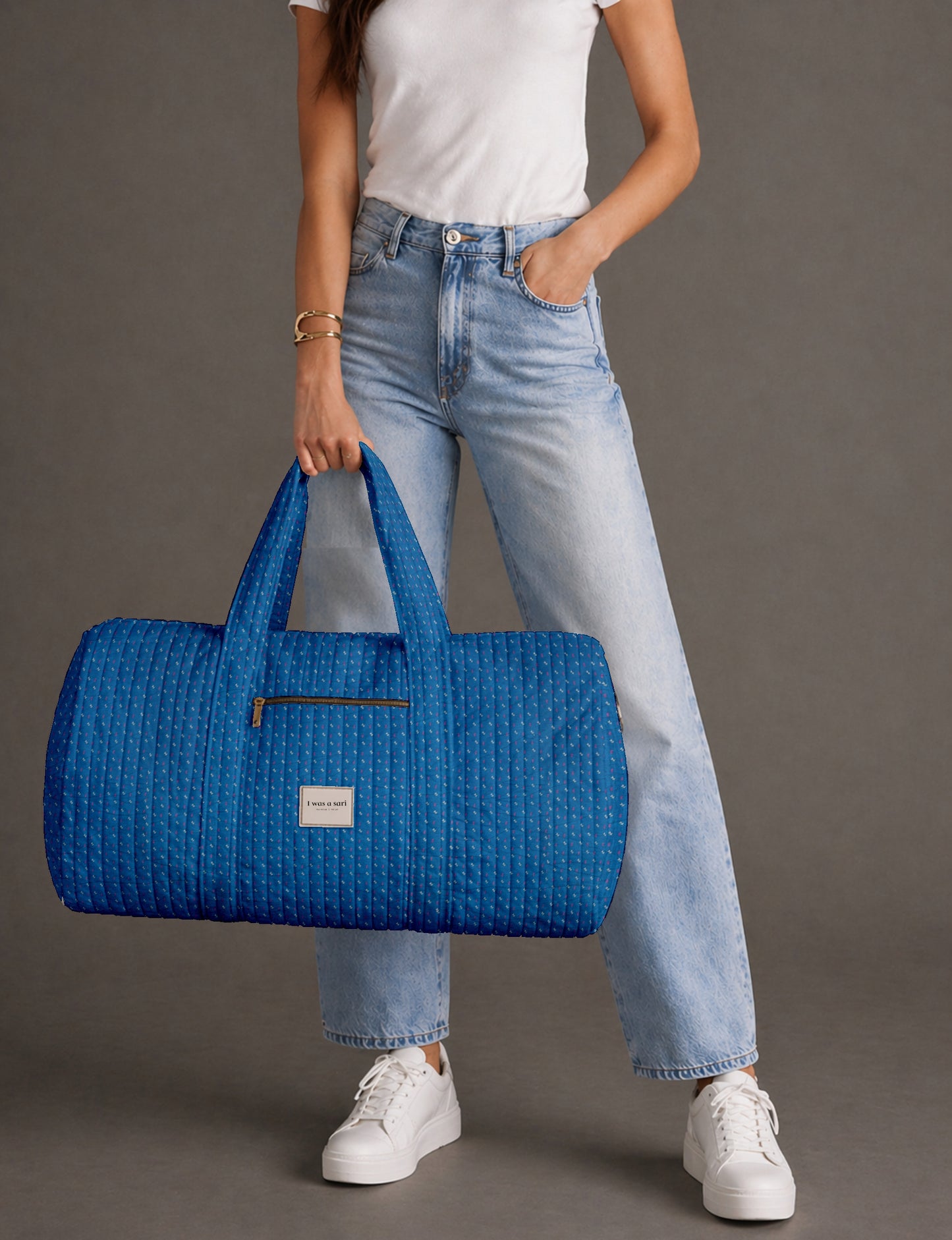 Woman holding a blue quilted barrel bag with micro pattern, front zipper pocket, and label "I was a sari" visible