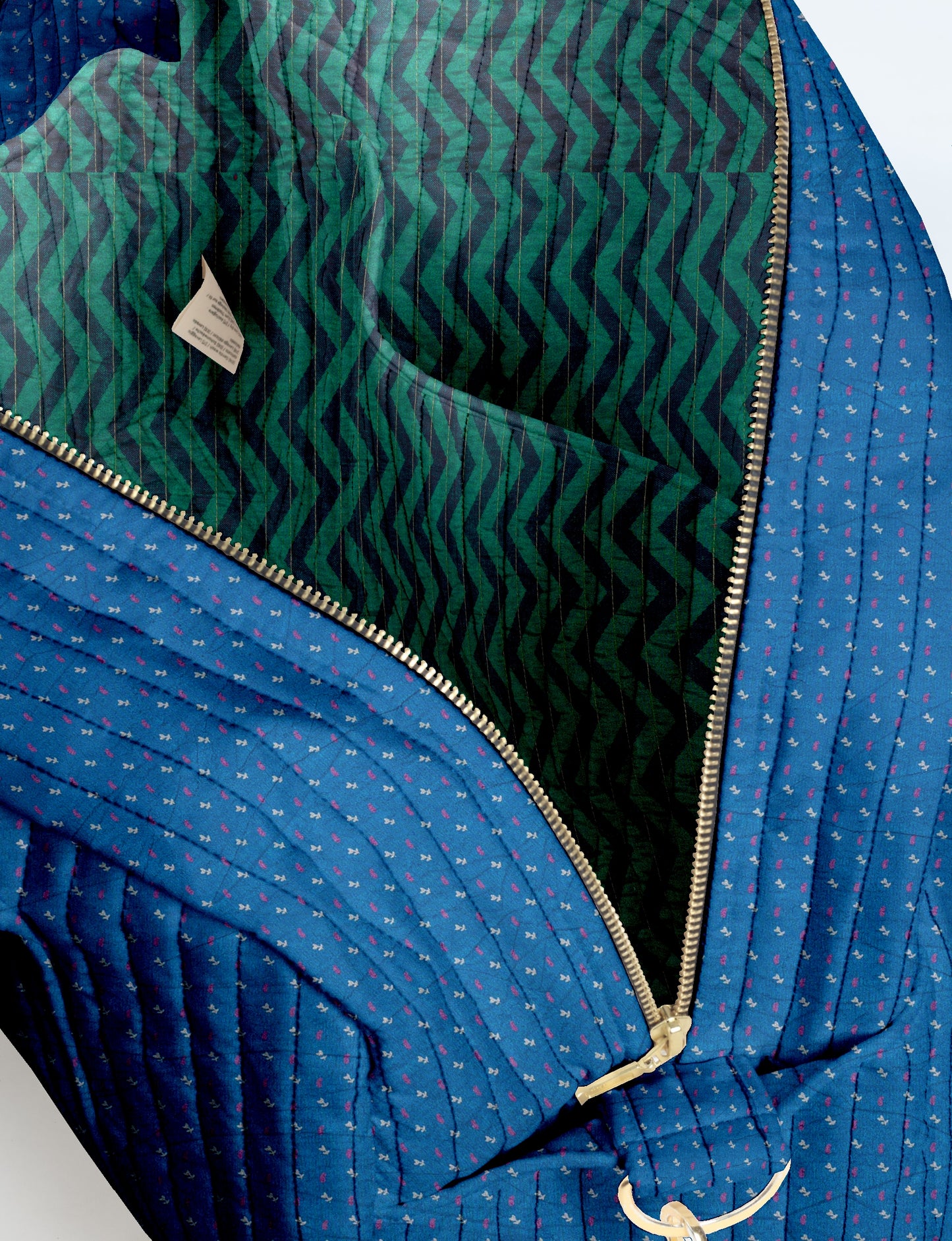 Blue quilted duffle bag with small pink and white floral print, gold zipper, and green and black chevron patterned interior