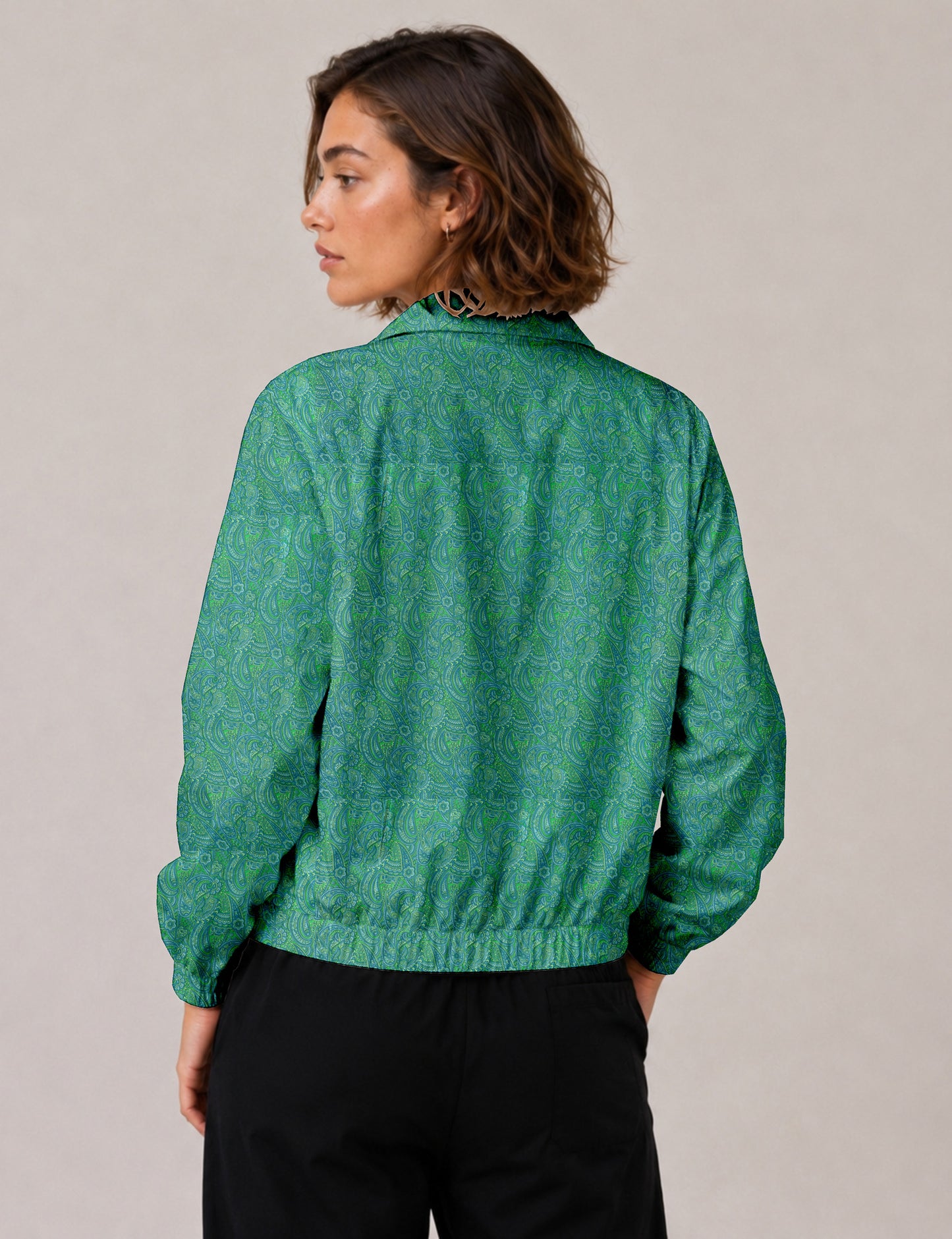 Woman wearing a blue and green paisley patterned bomber jacket with elastic cuffs and waistband, shown from the back