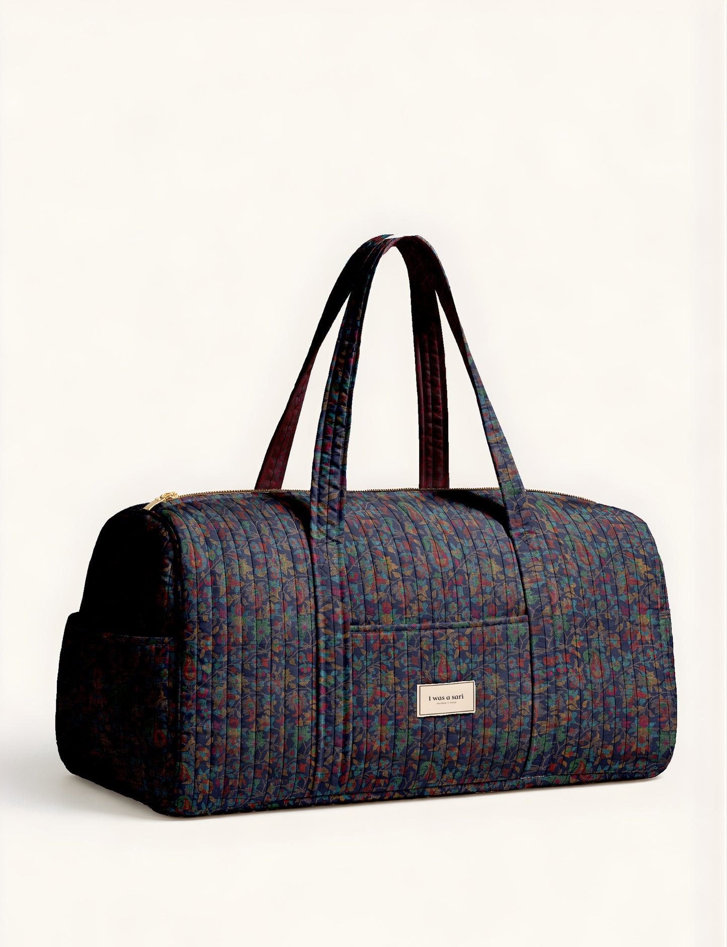 Woman holding a brown paisley quilted barrel bag with front zipper pocket, wearing light blue jeans and white sneakers