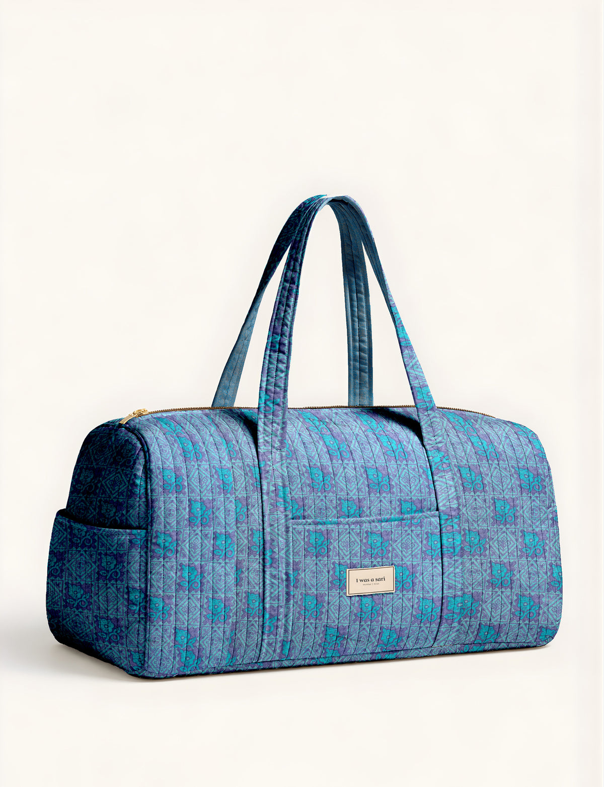 Woman holding a brown paisley quilted barrel bag with front zipper pocket, wearing light blue jeans and white sneakers