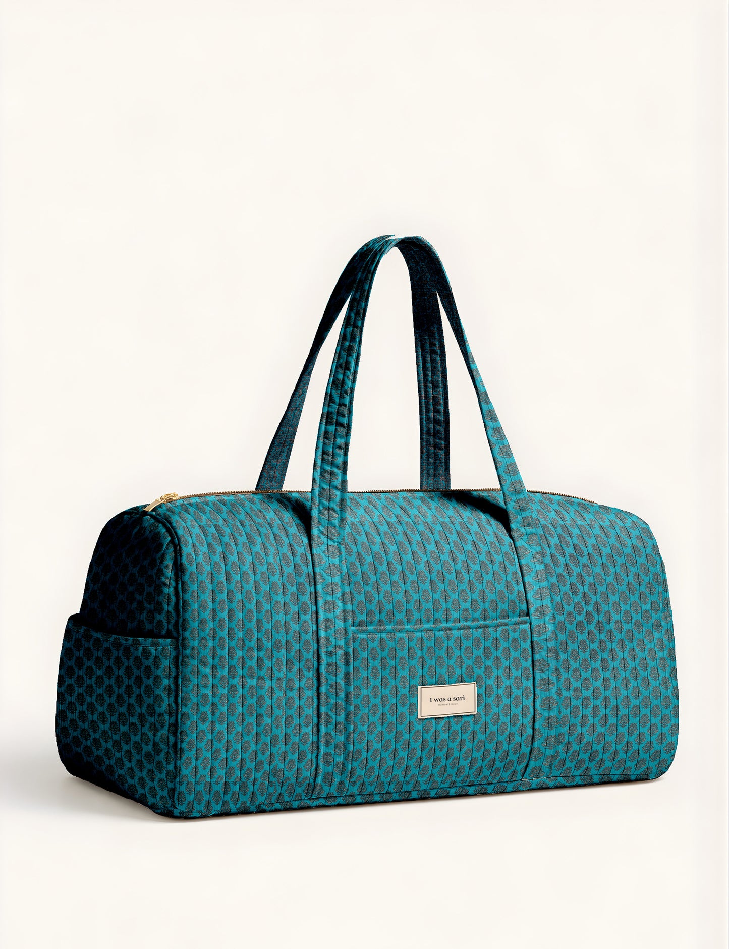 Quilted brown paisley barrel bag with double handles, front pocket, and gold zipper, shown in side angle view