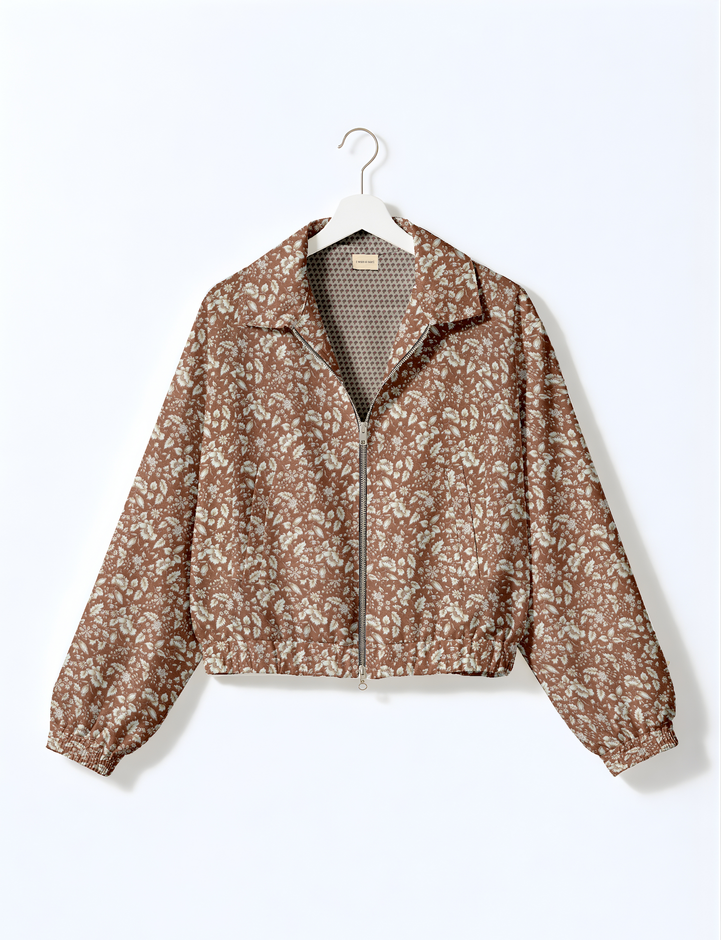 Brown floral bomber jacket with front zipper, elastic cuffs and waistband, hanging on white hanger, front view