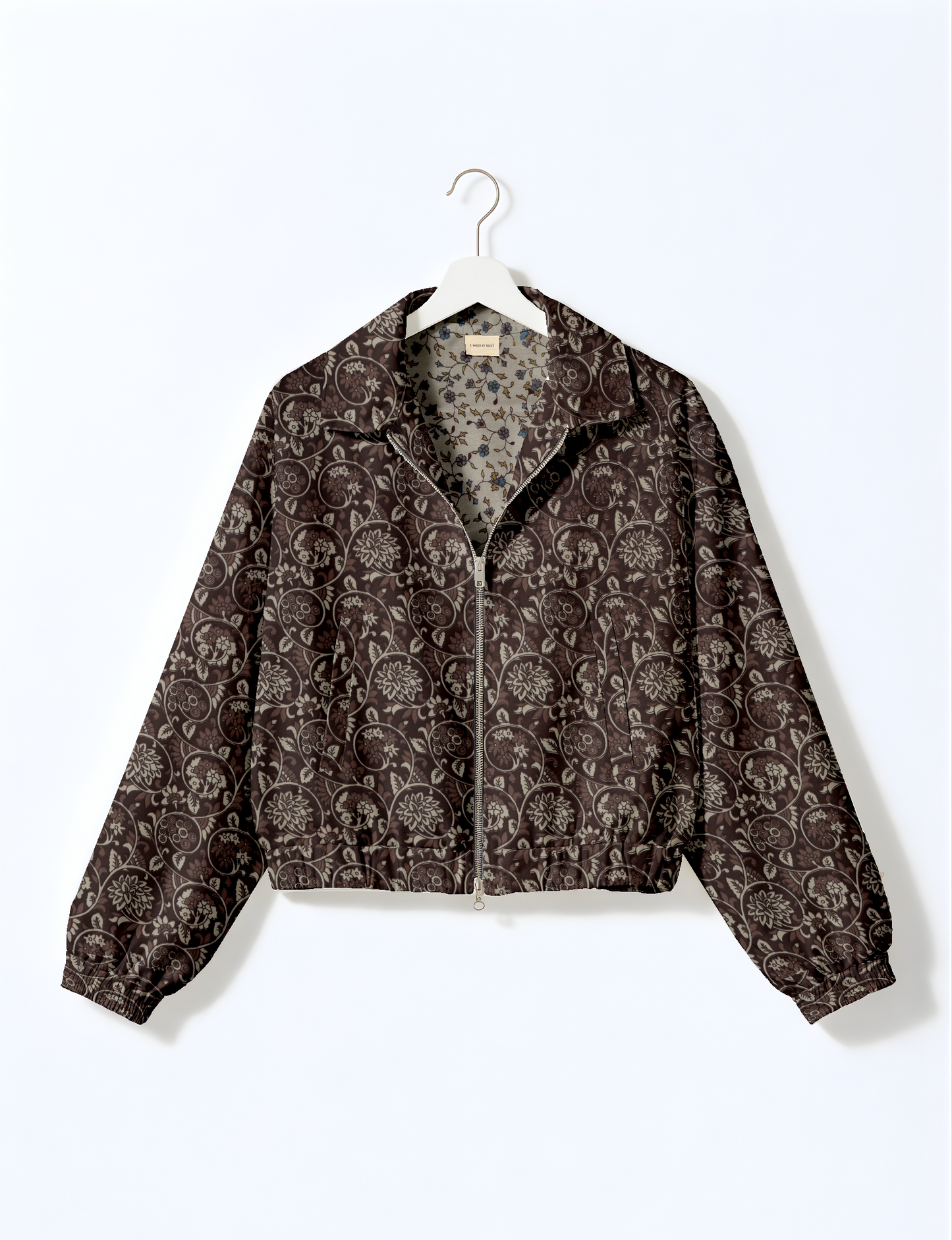 Brown floral bomber jacket with zipper front and elastic cuffs hanging on white hanger against white background