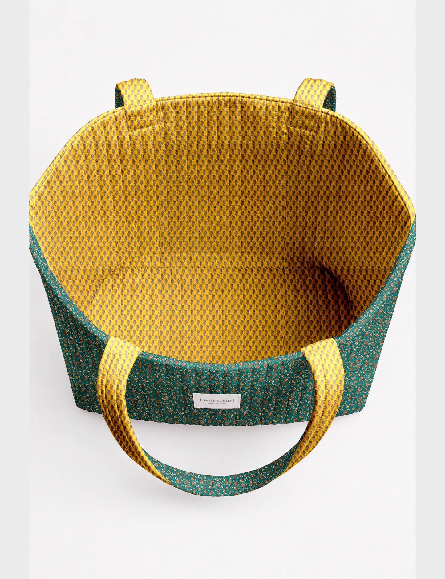 Quilted beach bag with yellow tropical exterior and red patterned interior, shown from top view with handles visible