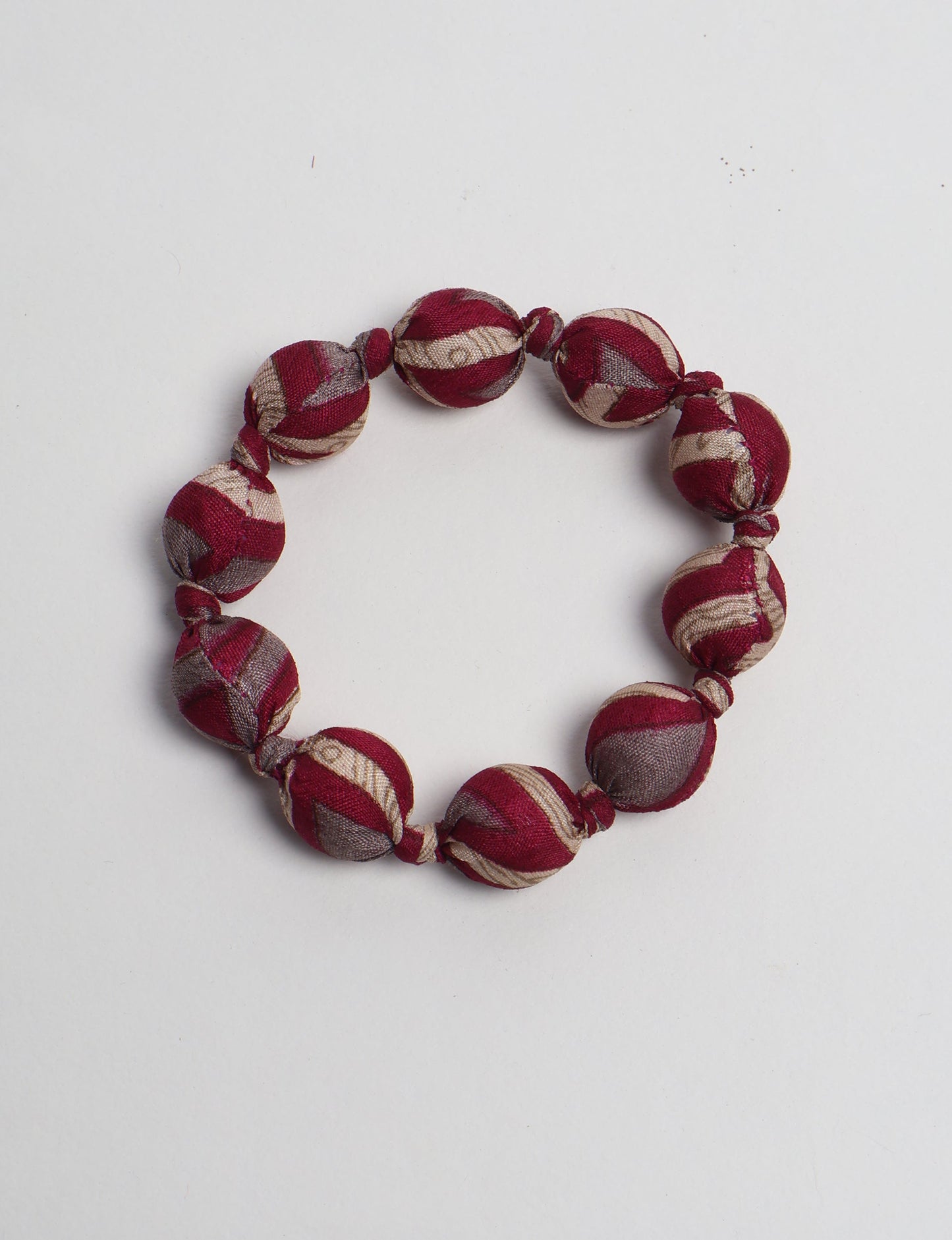 Red and beige striped fabric beaded bracelet with knotted details, shown flat on a white background