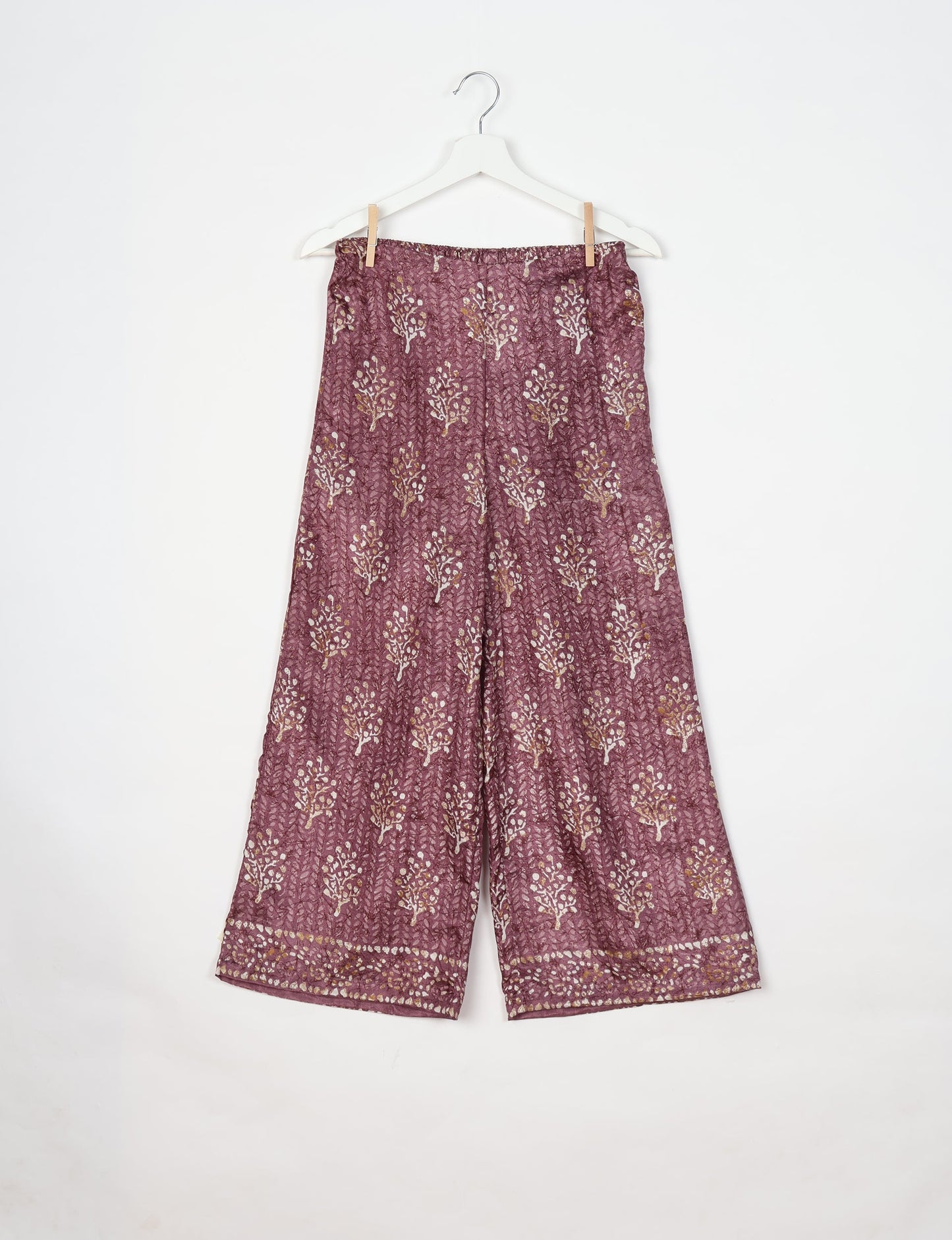 Purple tropical print wide-leg pants with elastic waistband hanging on white hanger against white background