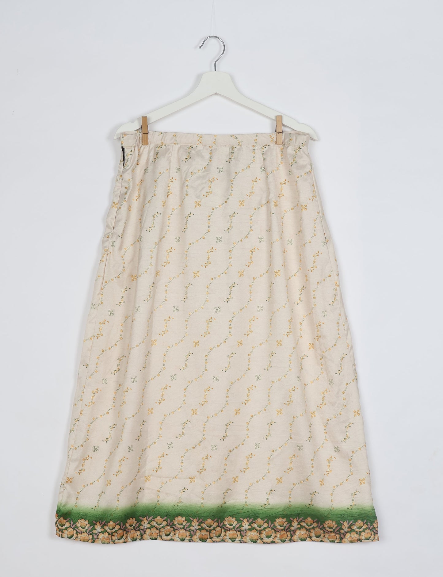 White A-line skirt with small yellow and green floral print and green floral border, hanging on white hanger