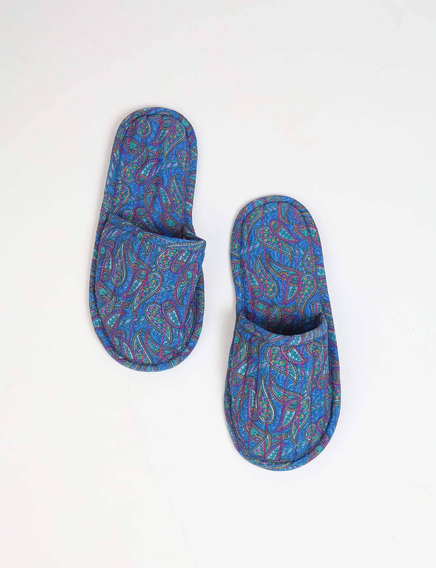 Blue quilted slippers with paisley pattern in shades of purple, green, and pink, shown from top view on white background