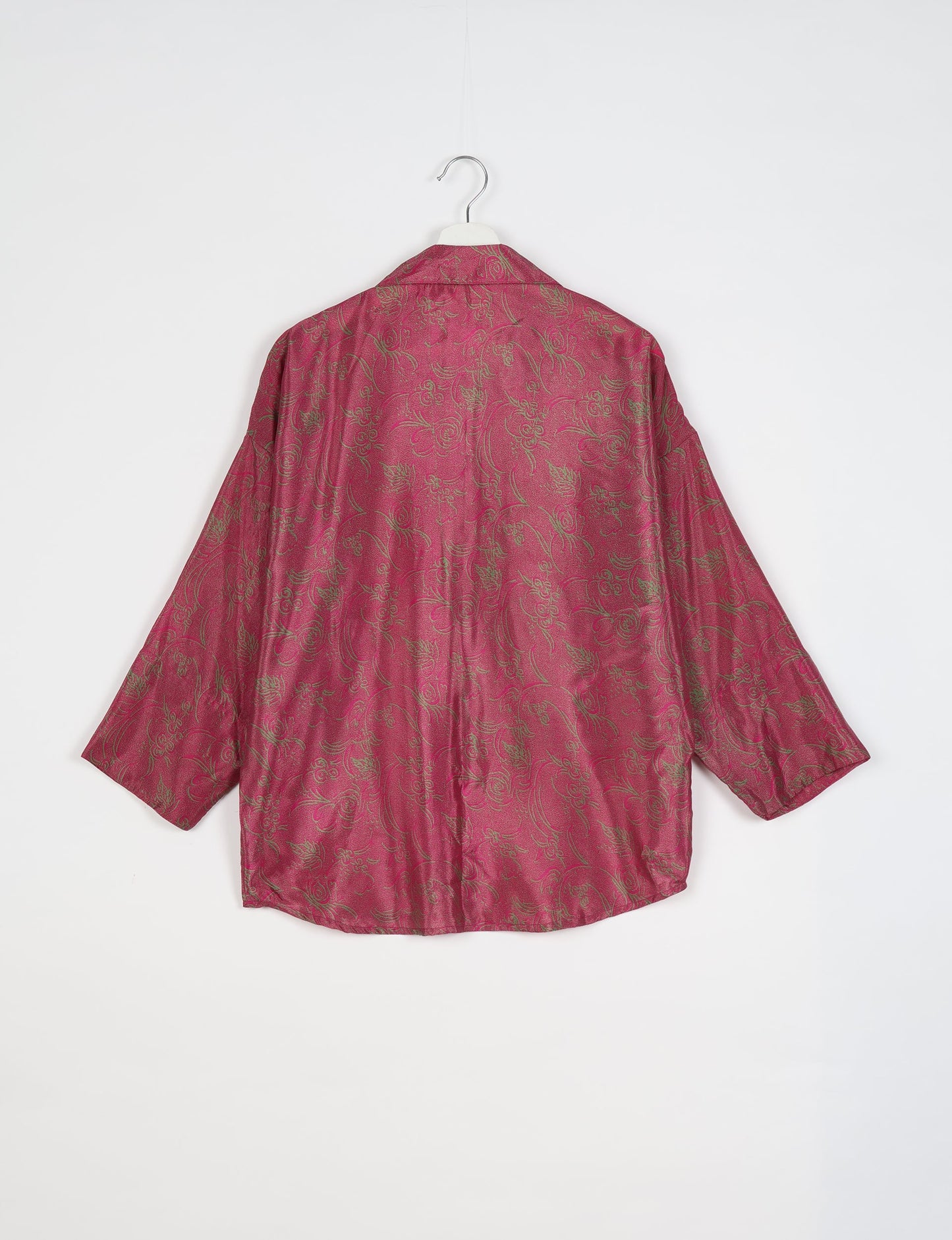 Oversized pink shirt with green tropical floral pattern, long sleeves, and spread collar, shown from back on hanger