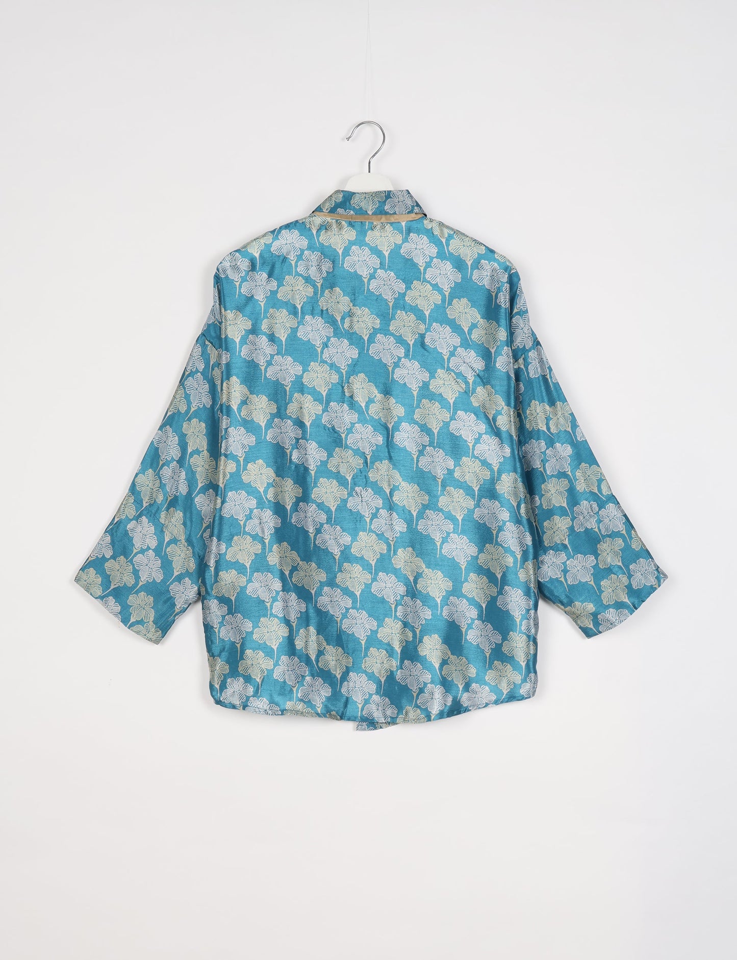 Blue oversized shirt with white and beige floral pattern, short sleeves, and collar, shown from back on hanger