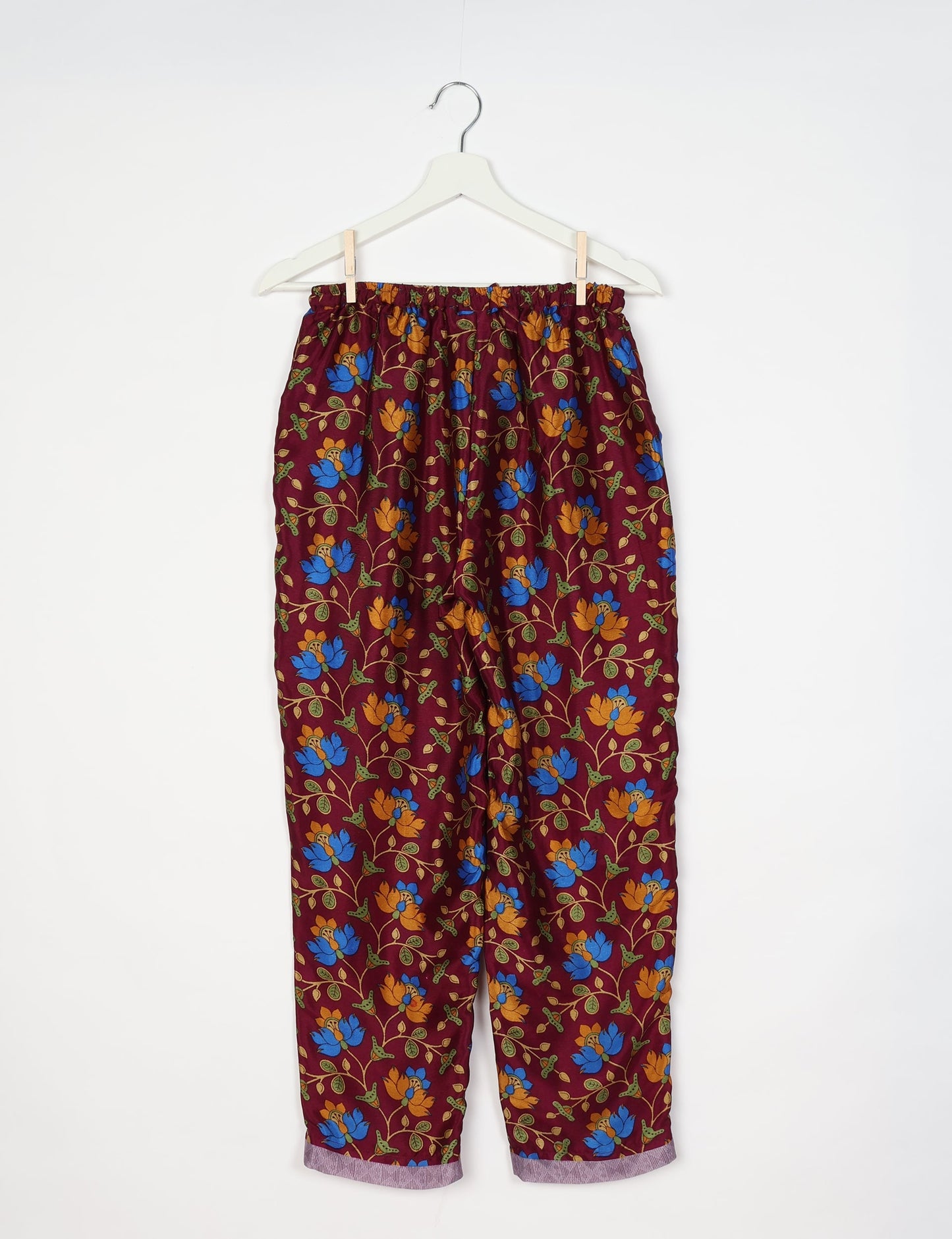 Red pull-on pants with blue and orange floral tropical print, elastic waistband, and cuffed hems hanging on white hanger