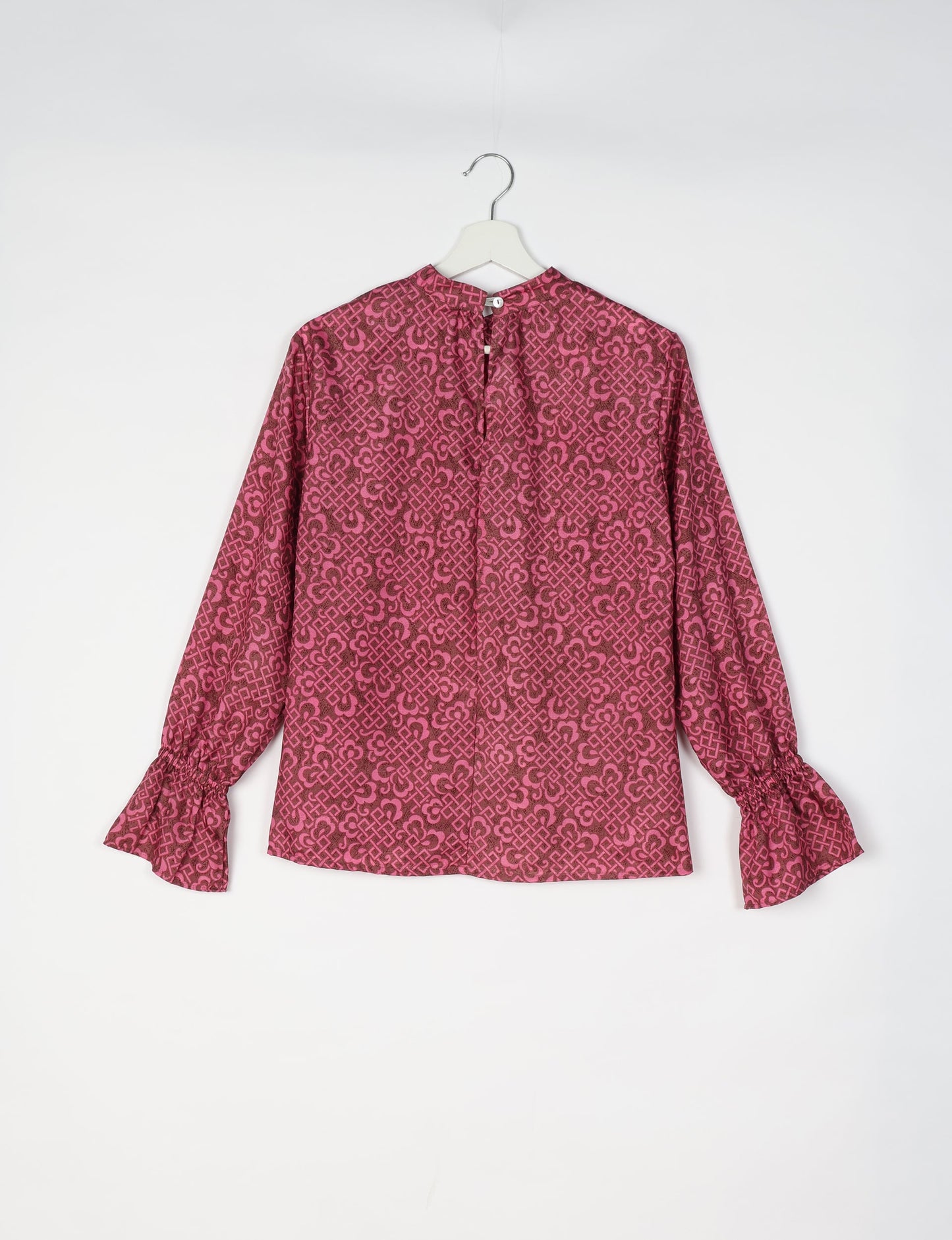 Pink and dark red patterned long-sleeve blouse with gathered cuffs and button closure at the back neckline, hanging on white
