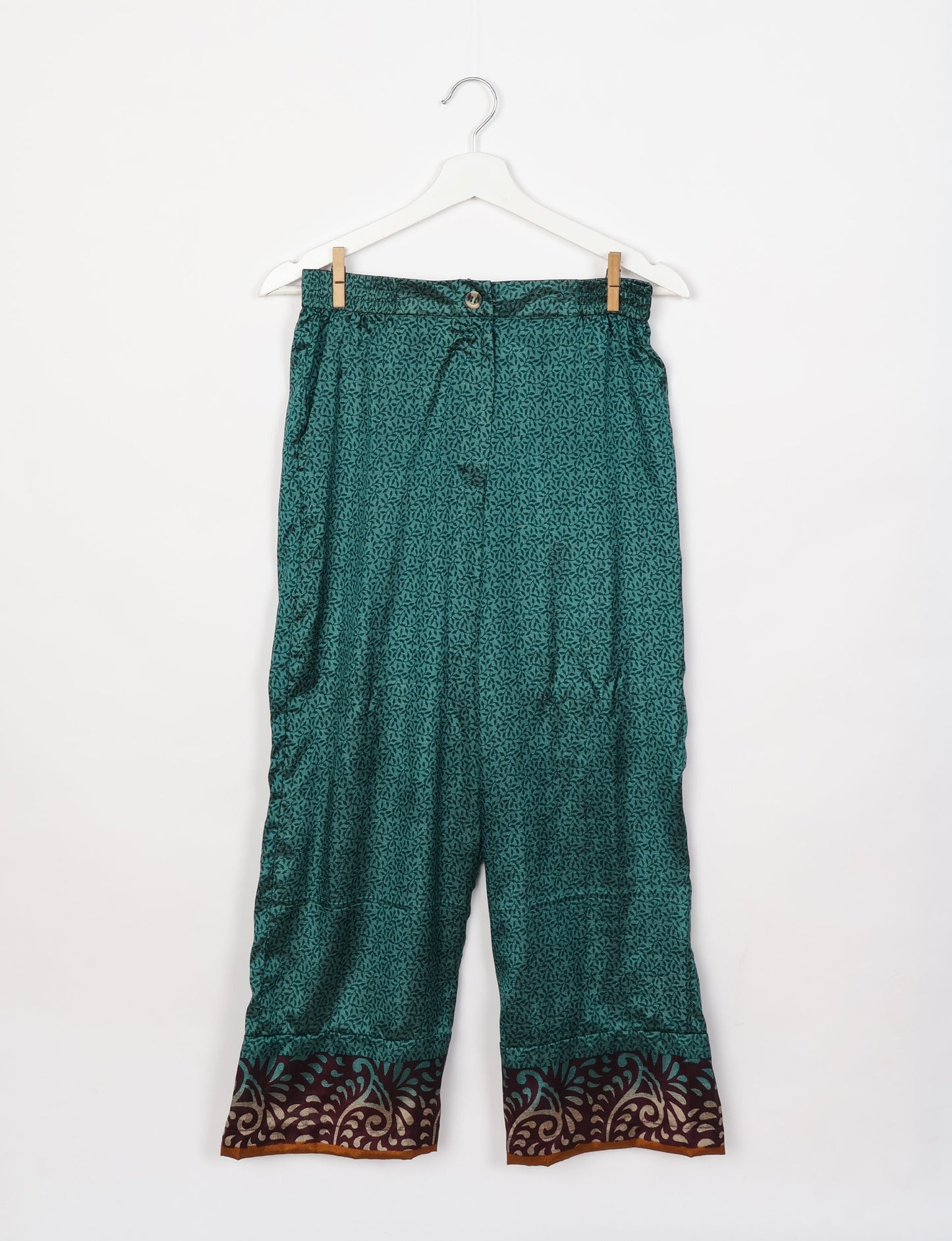 Green lounge pants with micro leaf pattern and contrasting dark brown and beige decorative border, hanging on white hanger