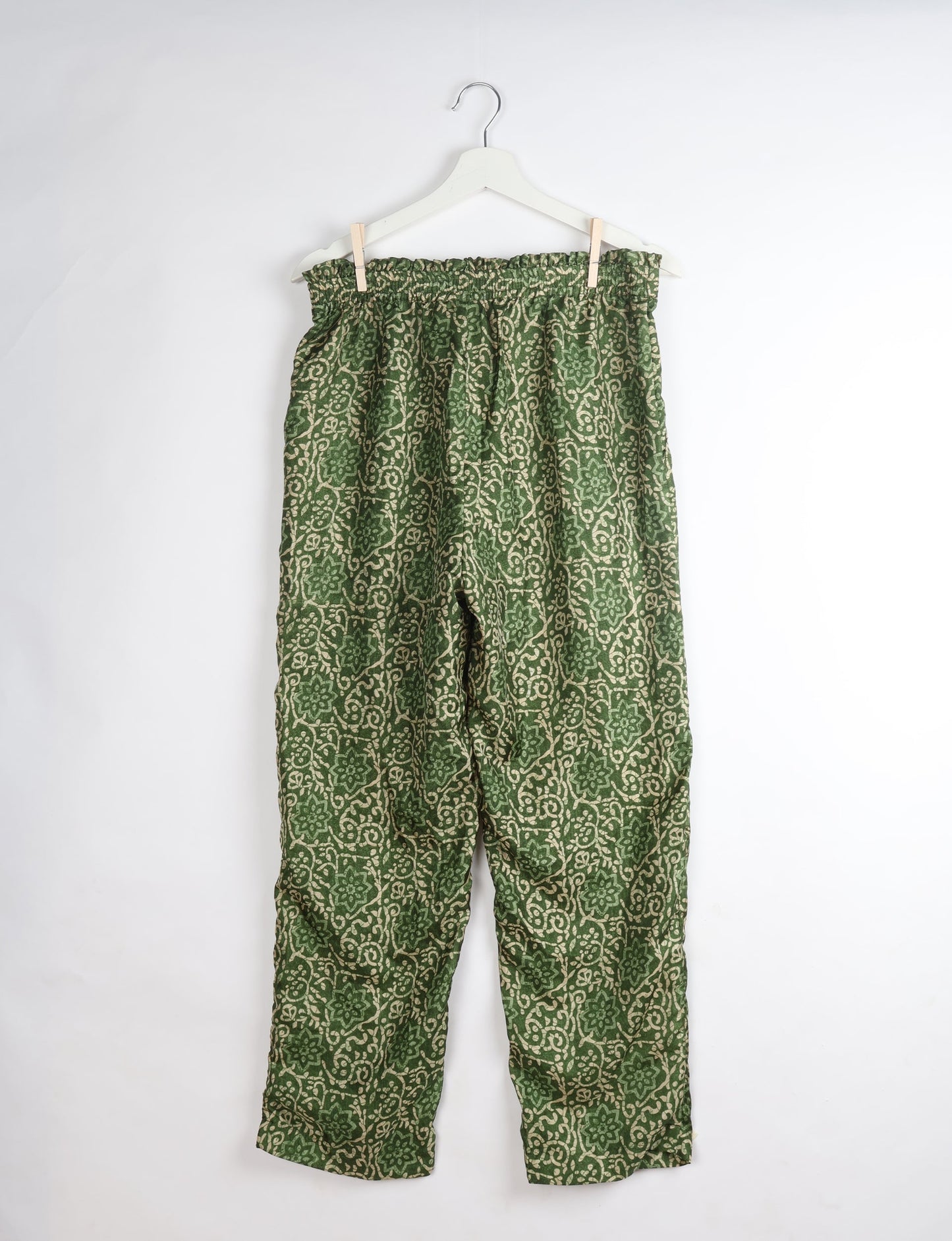 Green tropical print paperbag high-waisted pull-on pants hanging on white hanger against white background