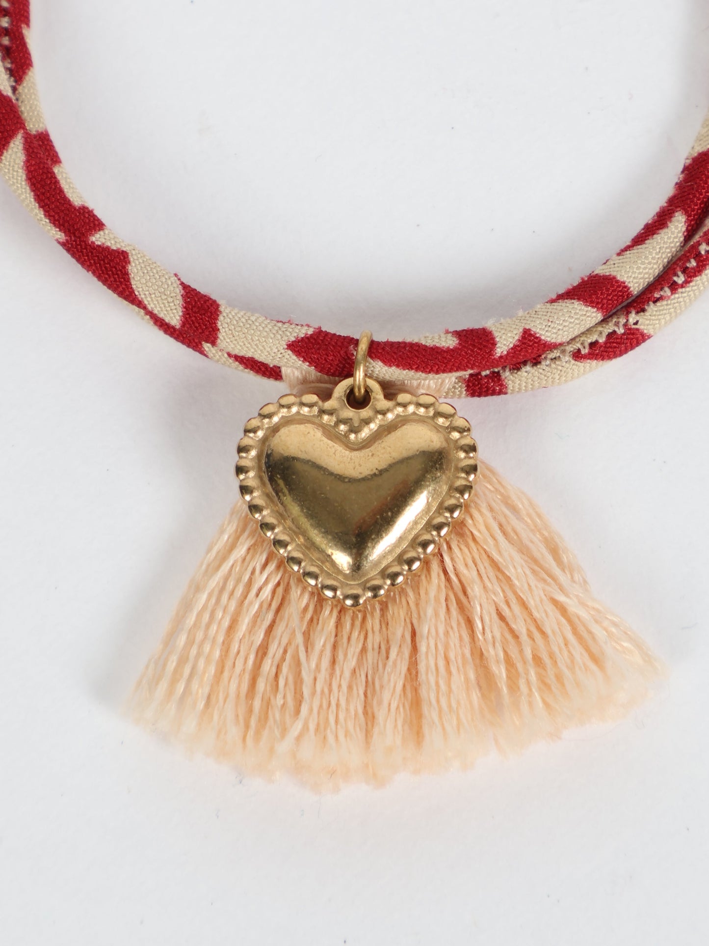 Handmade rope bracelet from recycled sari fabric with gold heart charm and tassels—eco friendly cloth, climate neutral fashion, and upcycled women’s clothing.