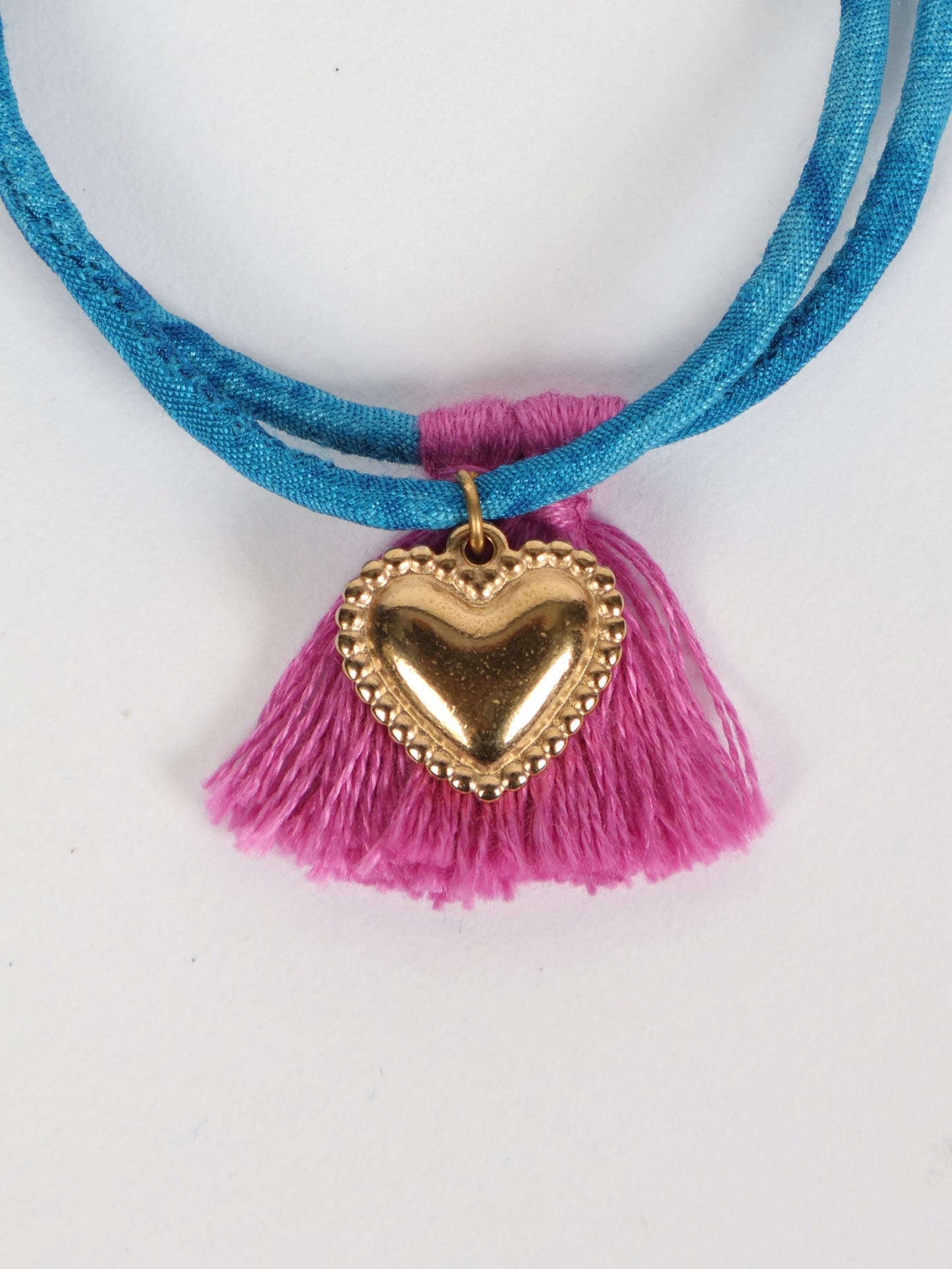 Handmade rope bracelet from recycled sari fabric with gold heart charm and tassels—eco friendly cloth, climate neutral fashion, and upcycled women’s clothing.