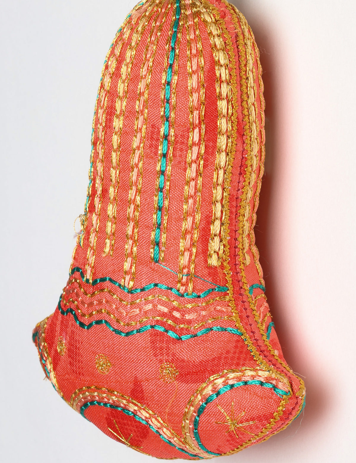 Close-up of a pink fabric bell ornament with gold, teal, and peach embroidered vertical stripes and floral patterns