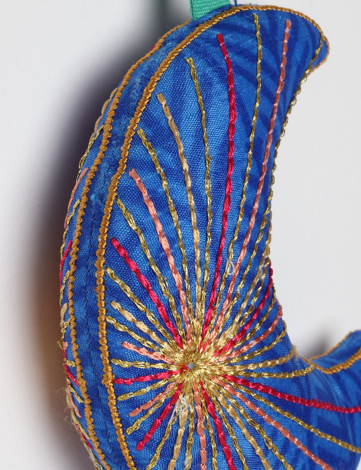 Blue fabric crescent moon ornament with multicolored stitched lines and a matching blue hanging loop against white background