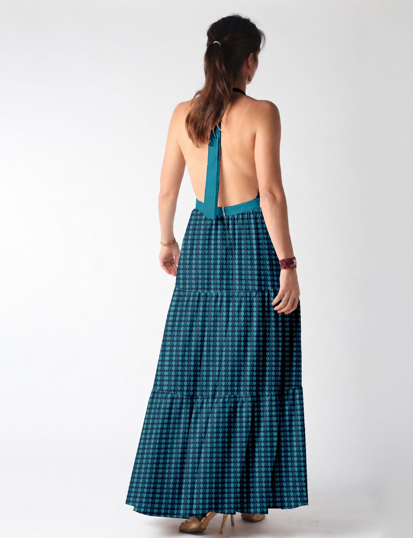 Woman wearing a blue tiered maxi dress with leaf pattern, halter neck, and open back, shown from the rear
