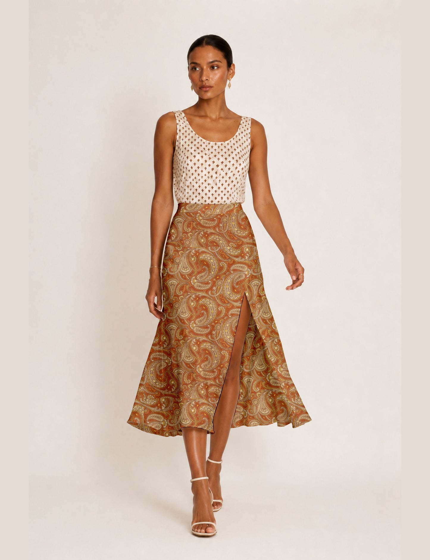 Woman wearing an orange paisley A-line skirt with a front slit, paired with a sleeveless beige patterned top, front view