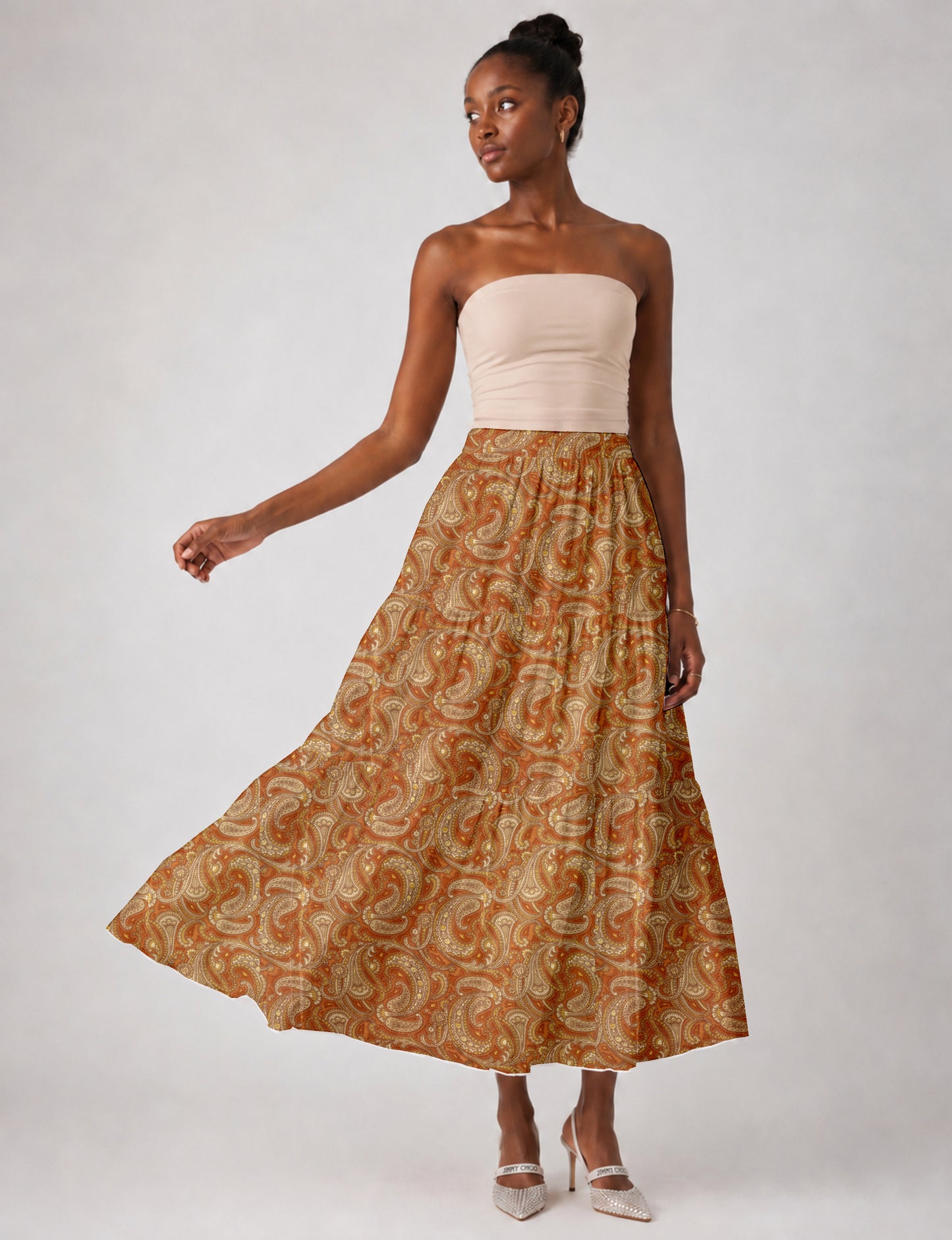 Woman wearing an orange paisley midi tiered skirt with a beige strapless top and white pointed heels, front view