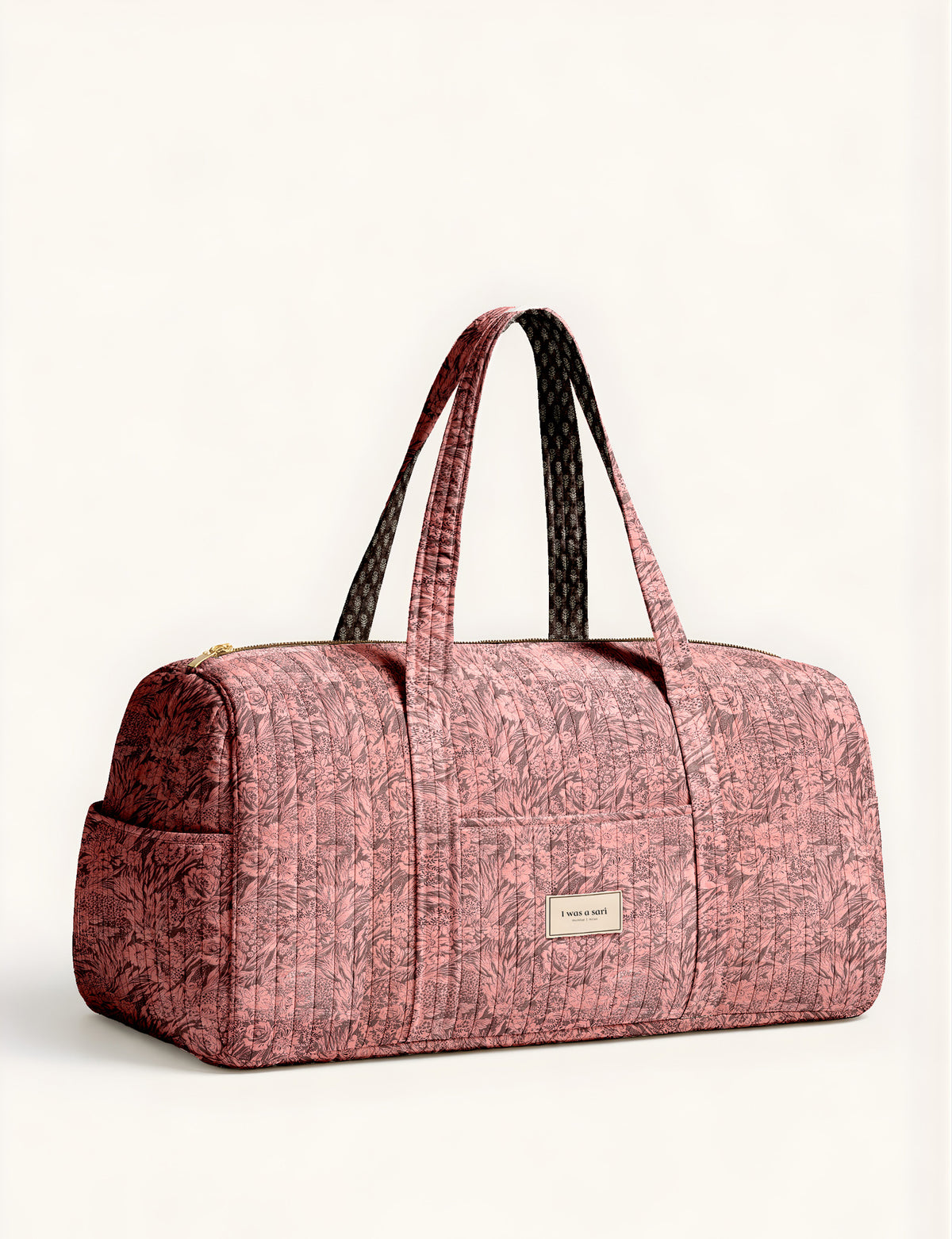 Woman holding a brown paisley quilted barrel bag with front zipper pocket, wearing light blue jeans and white sneakers