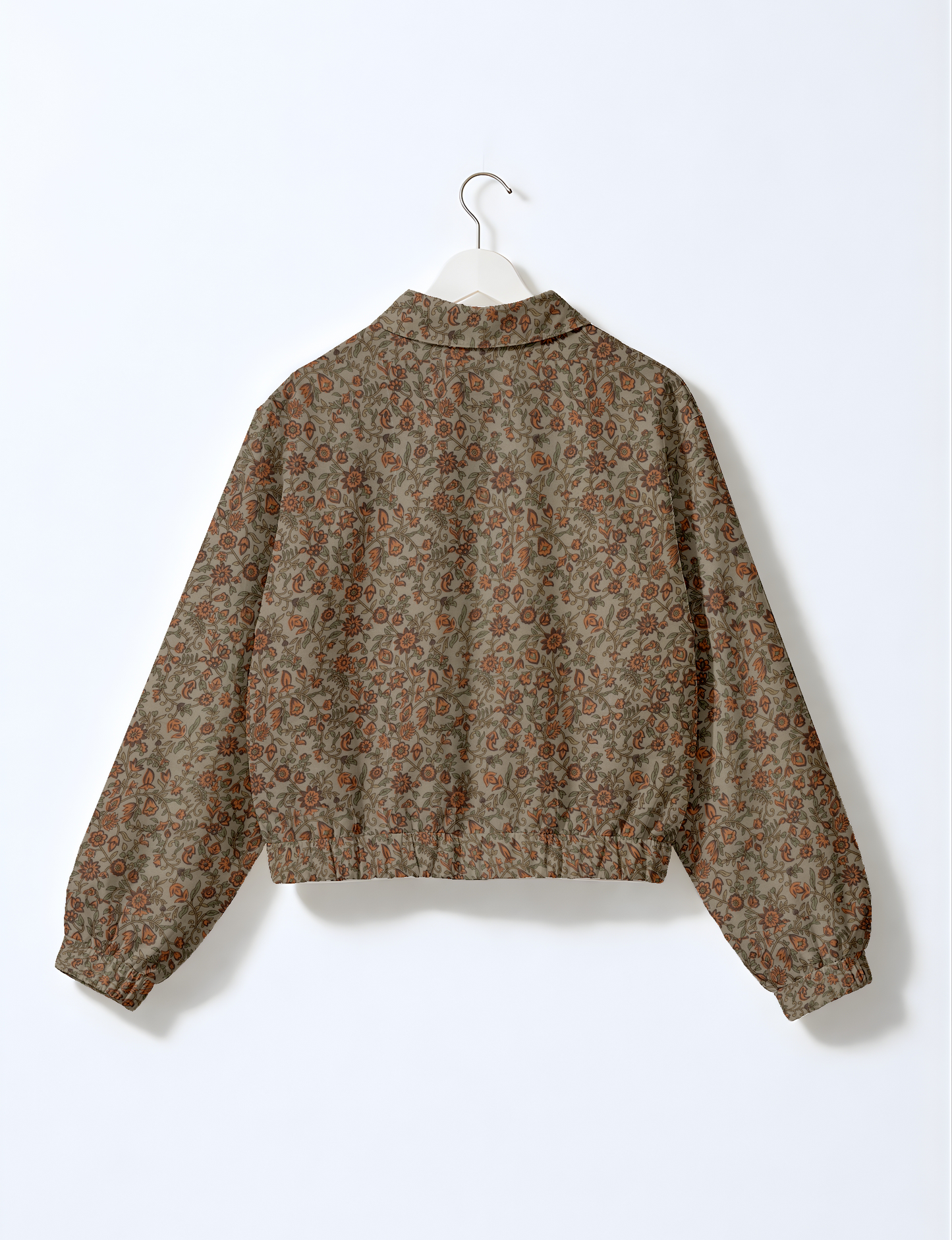 Back view of a floral patterned bomber jacket in muted pink and brown tones hanging on a white hanger against a white background