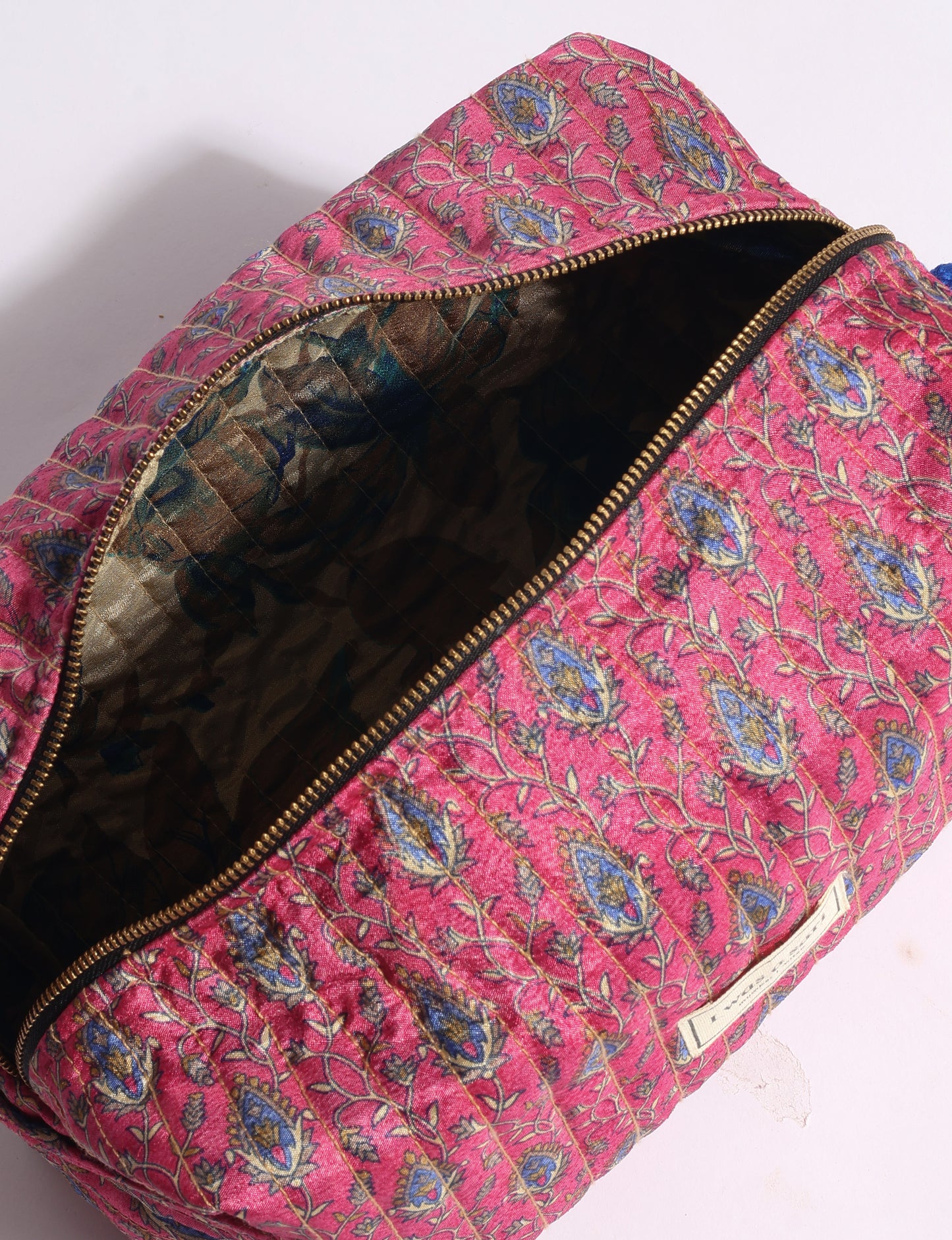 Quilted utility pouch in pink with blue and gold tropical floral print, open zipper showing dark patterned interior lining