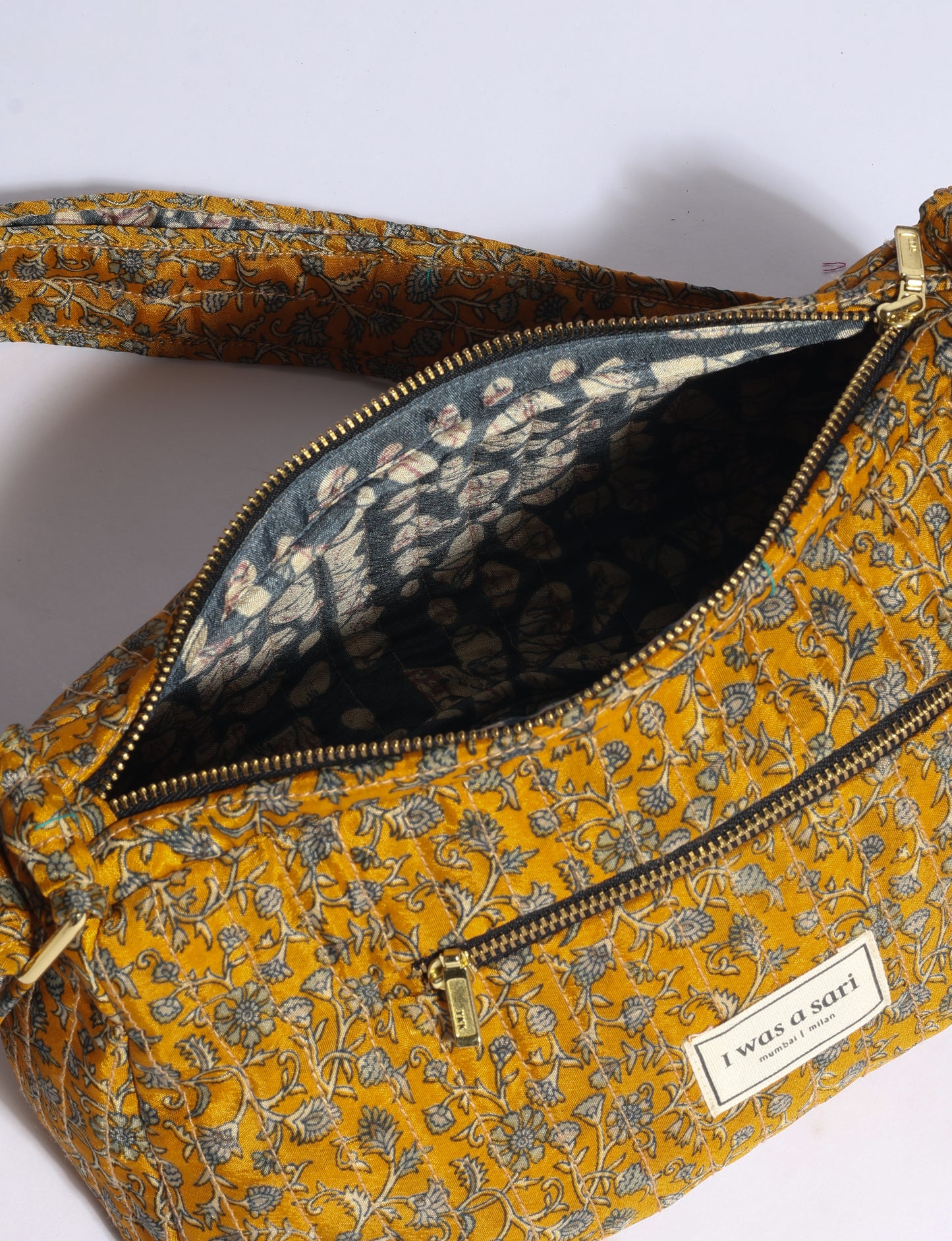 Quilted mustard yellow sling bag with floral print, gold zipper, front pocket, and "I was a sari" label, shown open from top