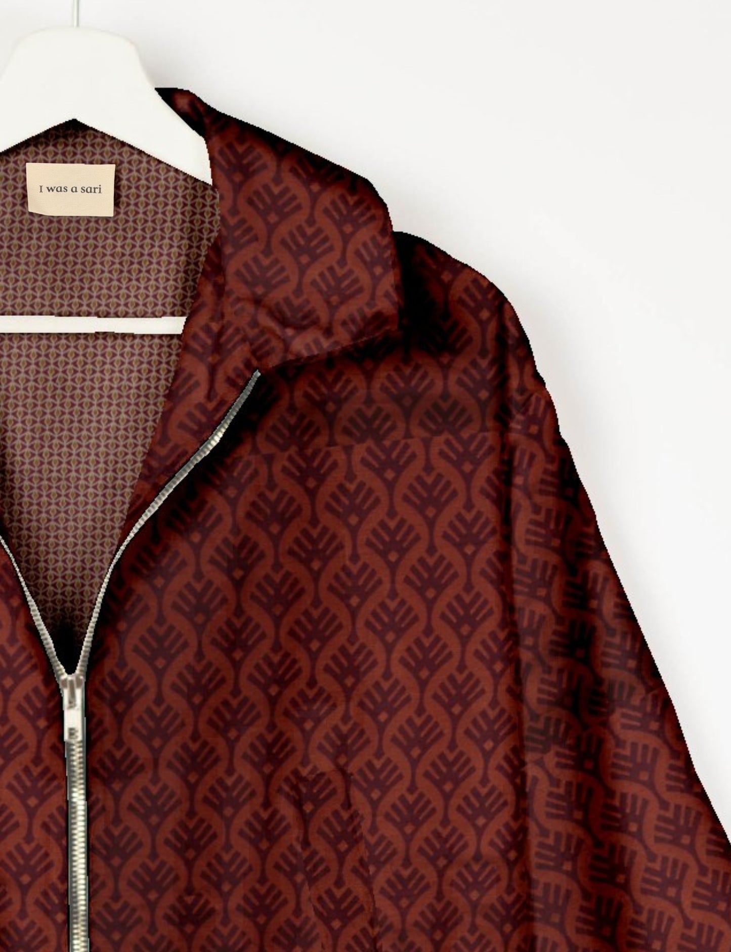 Red bomber jacket with dark leaf pattern, silver zipper, and inner label reading "I was a sari" on white hanger