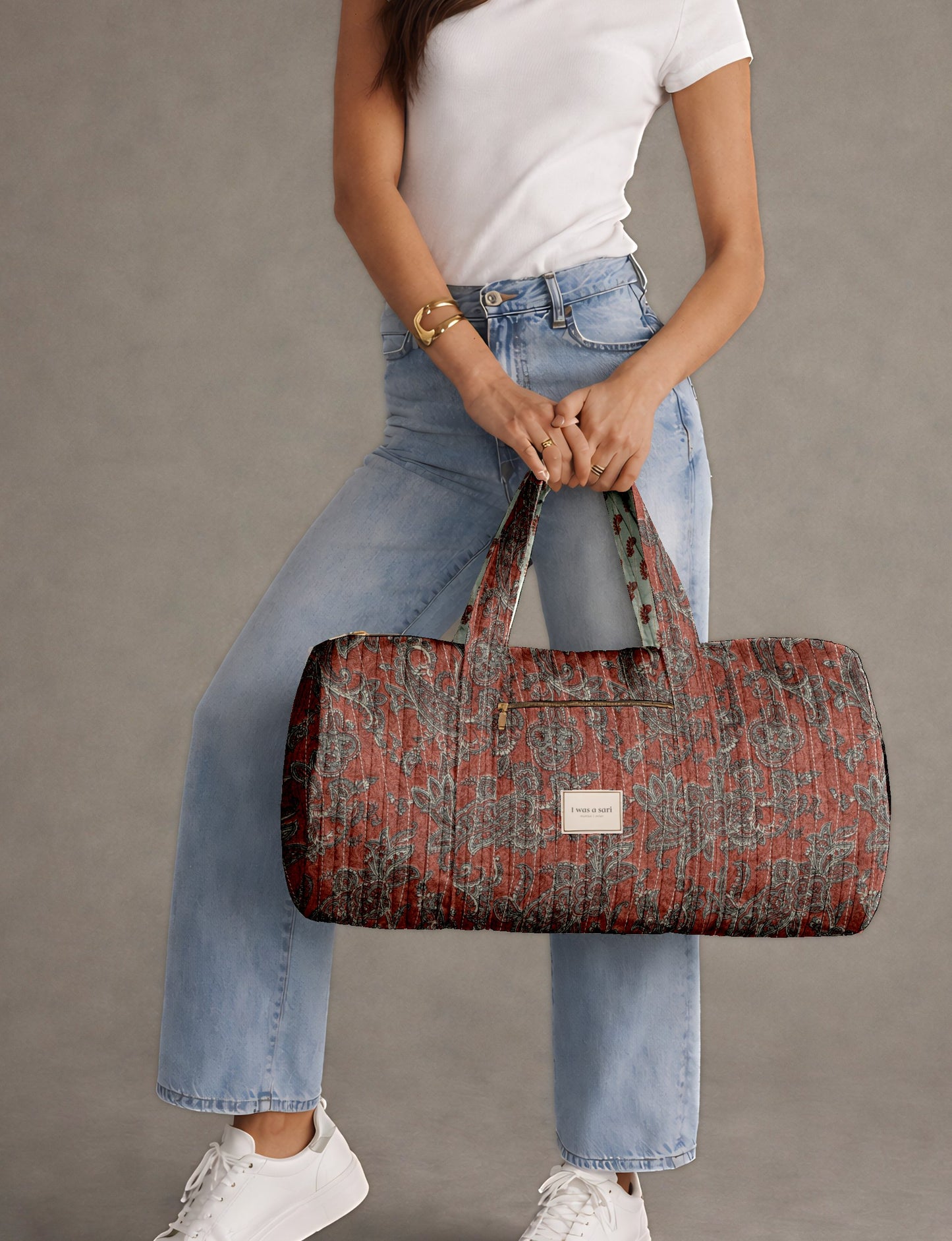 Woman wearing white t-shirt and light blue jeans holding a red paisley quilted bowling bag with front zipper pocket