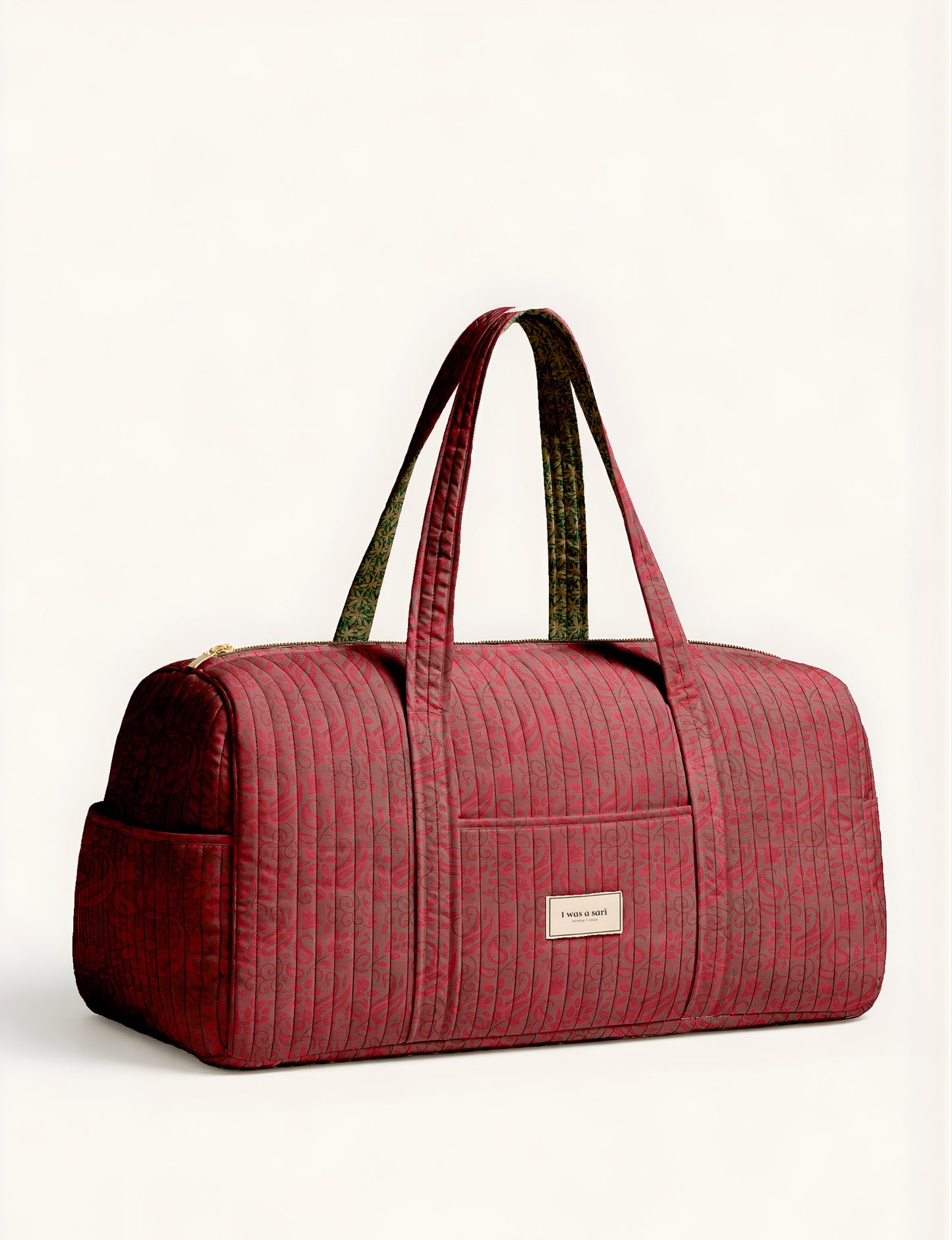 Woman holding a brown paisley quilted barrel bag with front zipper pocket, wearing light blue jeans and white sneakers