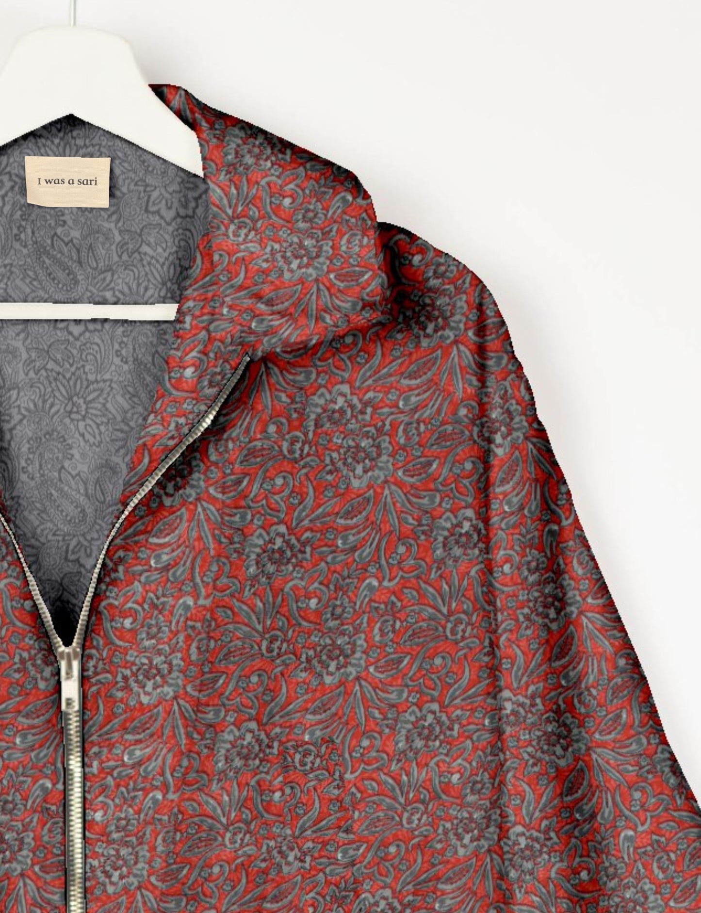 Red bomber jacket with gray floral tropical pattern, silver zipper, and inner gray paisley lining on white hanger