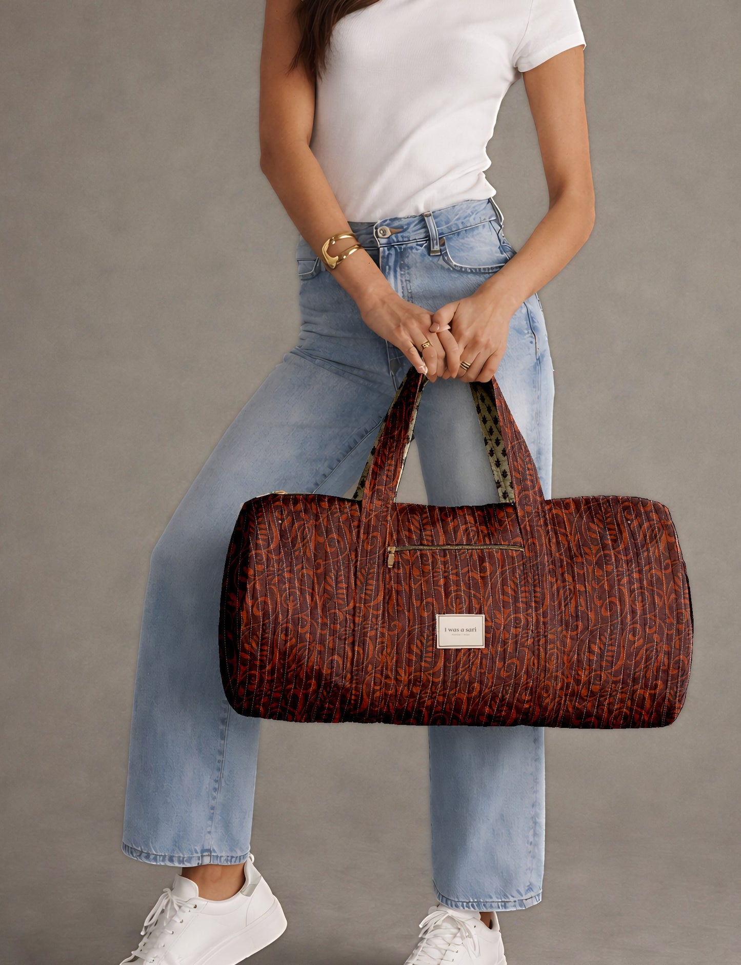 Quilted bowling bag by I Was A Sari with a structured design, featuring dual handles, zip closure, and a spacious interior with an outer zip pocket. Designed for everyday use and travel, it showcases a sleek elongated silhouette with functional storage and easy access compartments. Made from upcycled fabric, this sustainable handbag combines style and practicality, presented through detailed front, side, and lifestyle views.