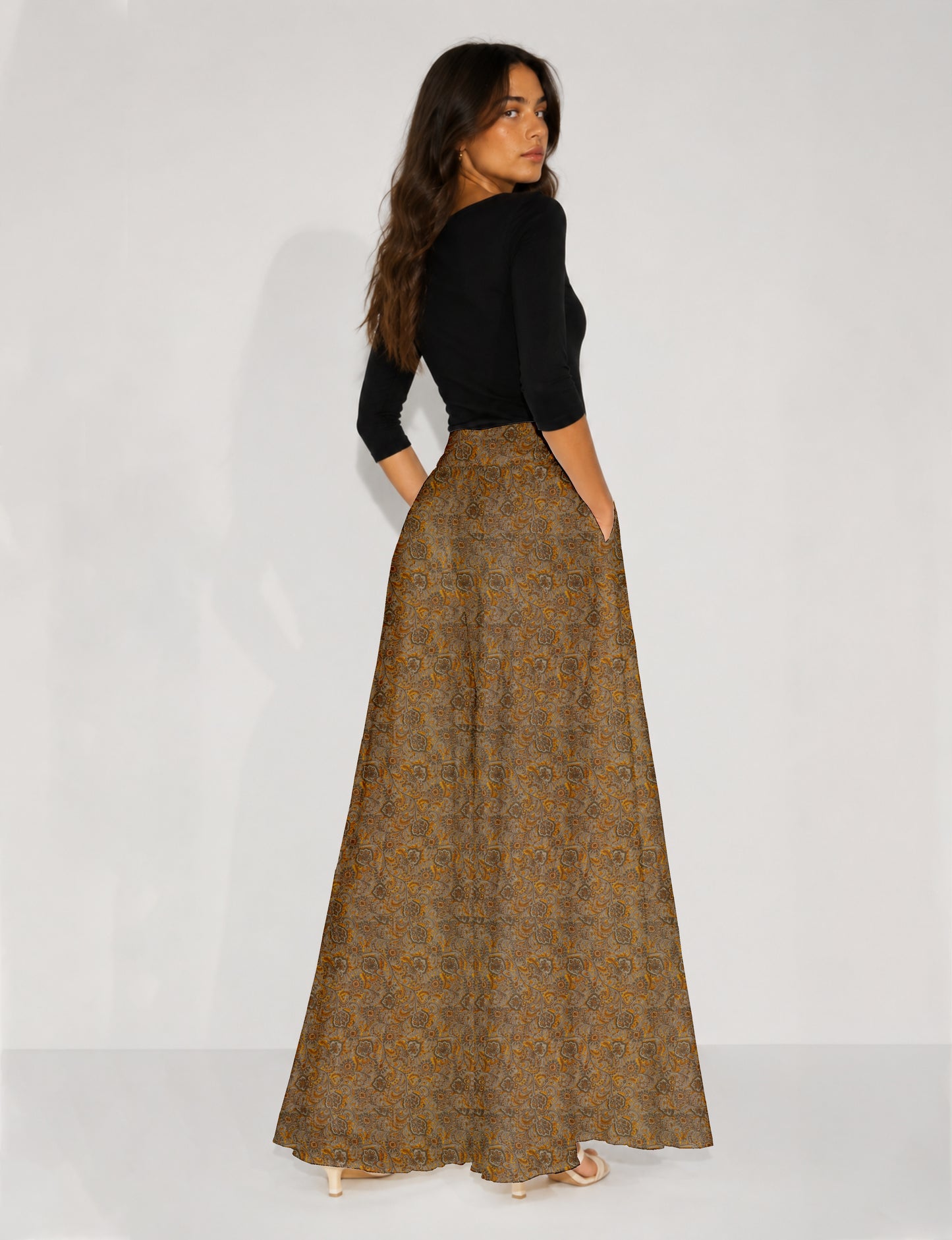 Woman wearing blue wide leg palazzo trousers with black and brown tropical floral print, side pockets, shown from back angle