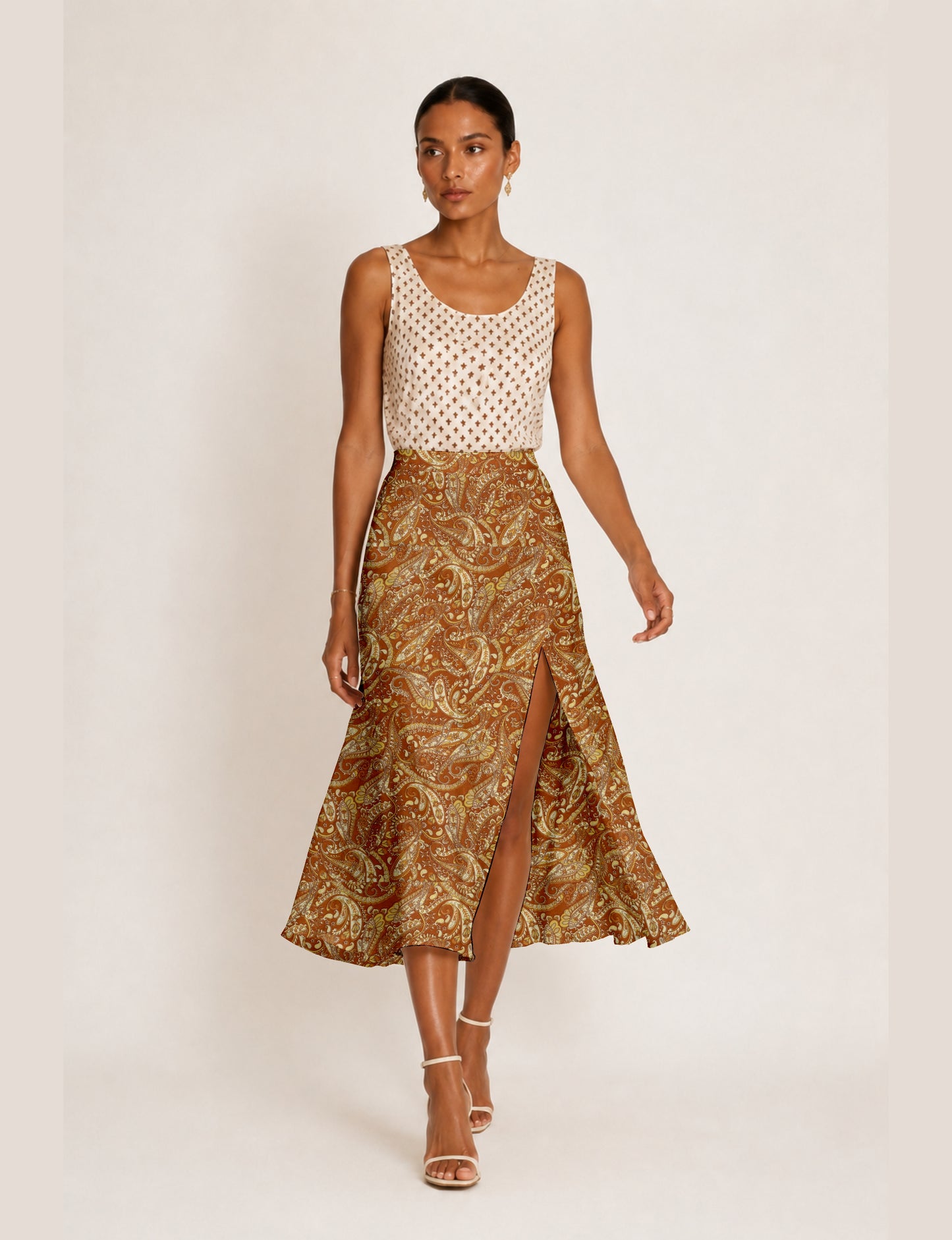 Woman wearing a yellow paisley A-line skirt with a front slit, paired with a sleeveless white patterned top and beige heels