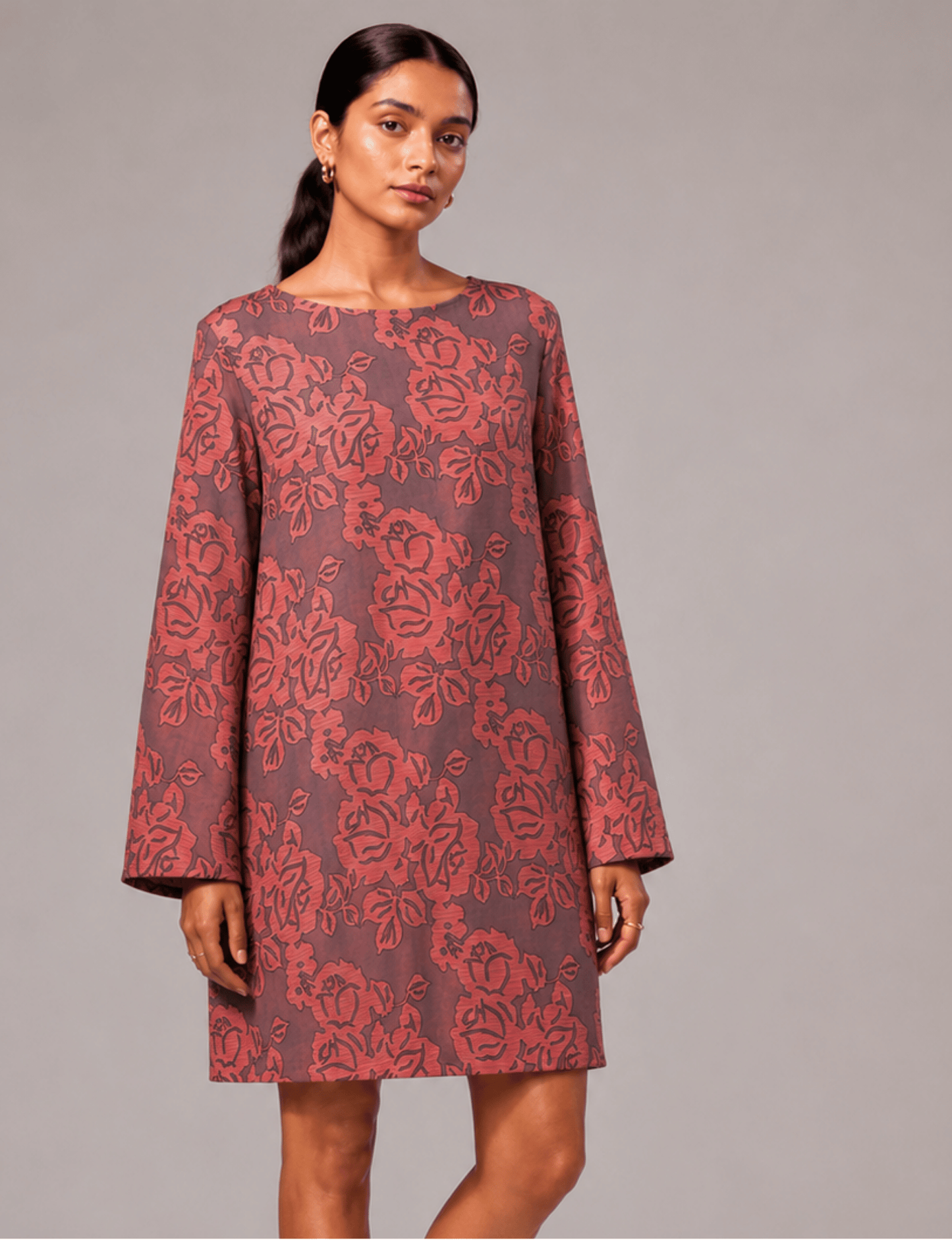 Model wearing a grey swing dress with large red floral print, long sleeves, and a round neckline, front view