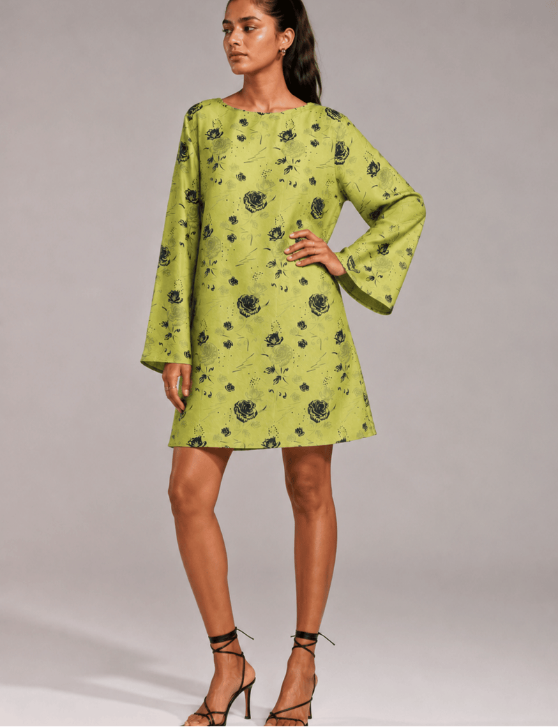 Model wearing a green floral swing dress with long bell sleeves and a round neckline, paired with black strappy heels