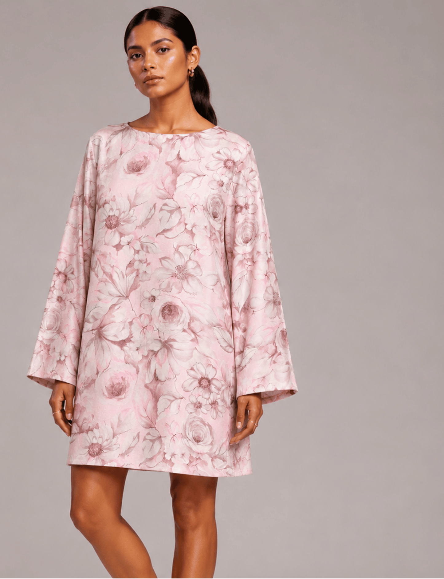 Woman wearing a pink floral swing dress with long sleeves and a round neckline, front view on a plain background