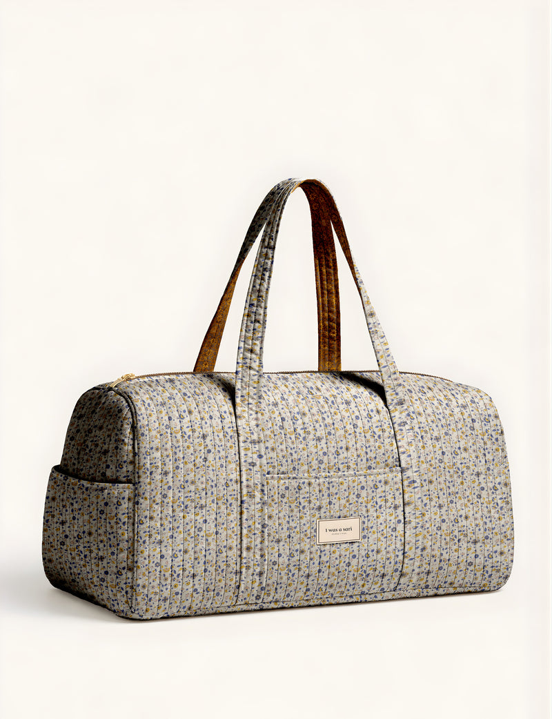 Woman holding a brown paisley quilted barrel bag with front zipper pocket, wearing light blue jeans and white sneakers