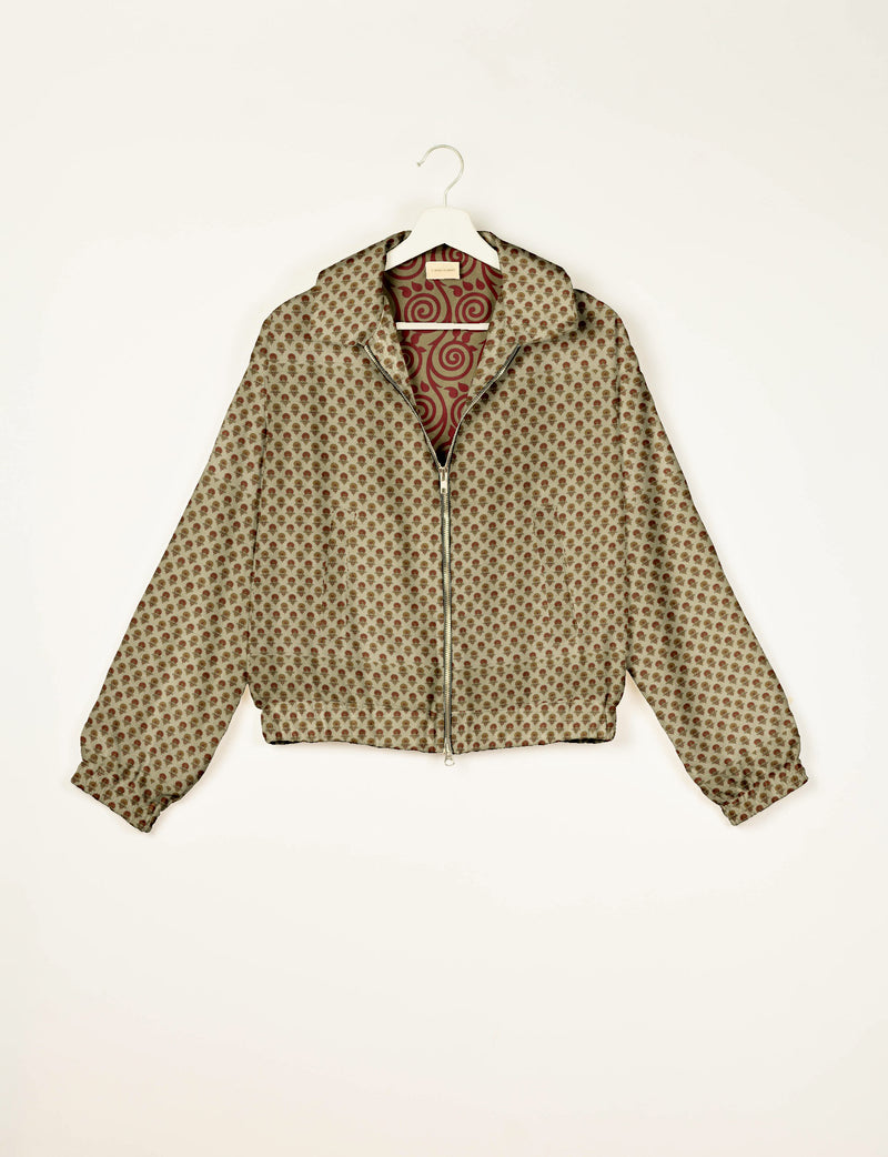Beige bomber jacket with small brown floral pattern, front zipper, collar, elastic cuffs, and red swirl patterned lining, on